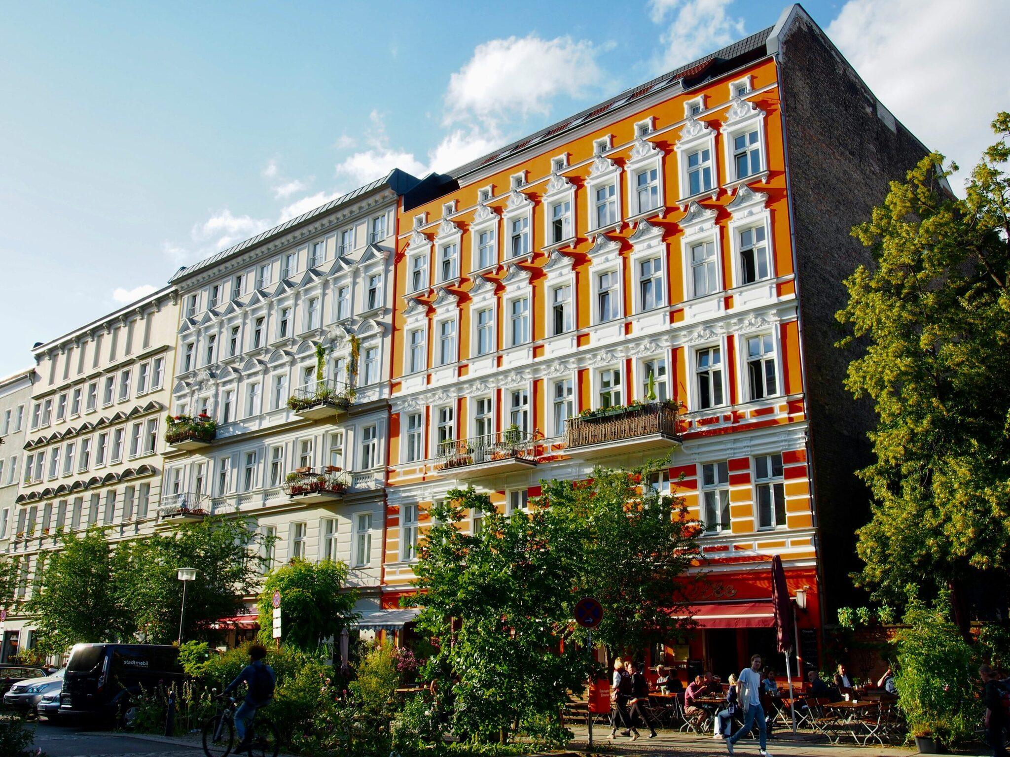A colourful Gründerzeit-style building with an orange and red facade, a lively ground-floor terrace and ivy-covered sides