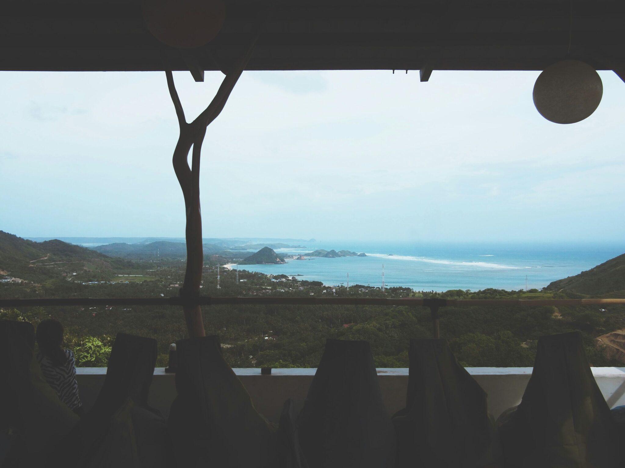 Vue panoramique depuis une terrasse sur une baie turquoise entourée de collines verdoyantes et de montagnes côtières
