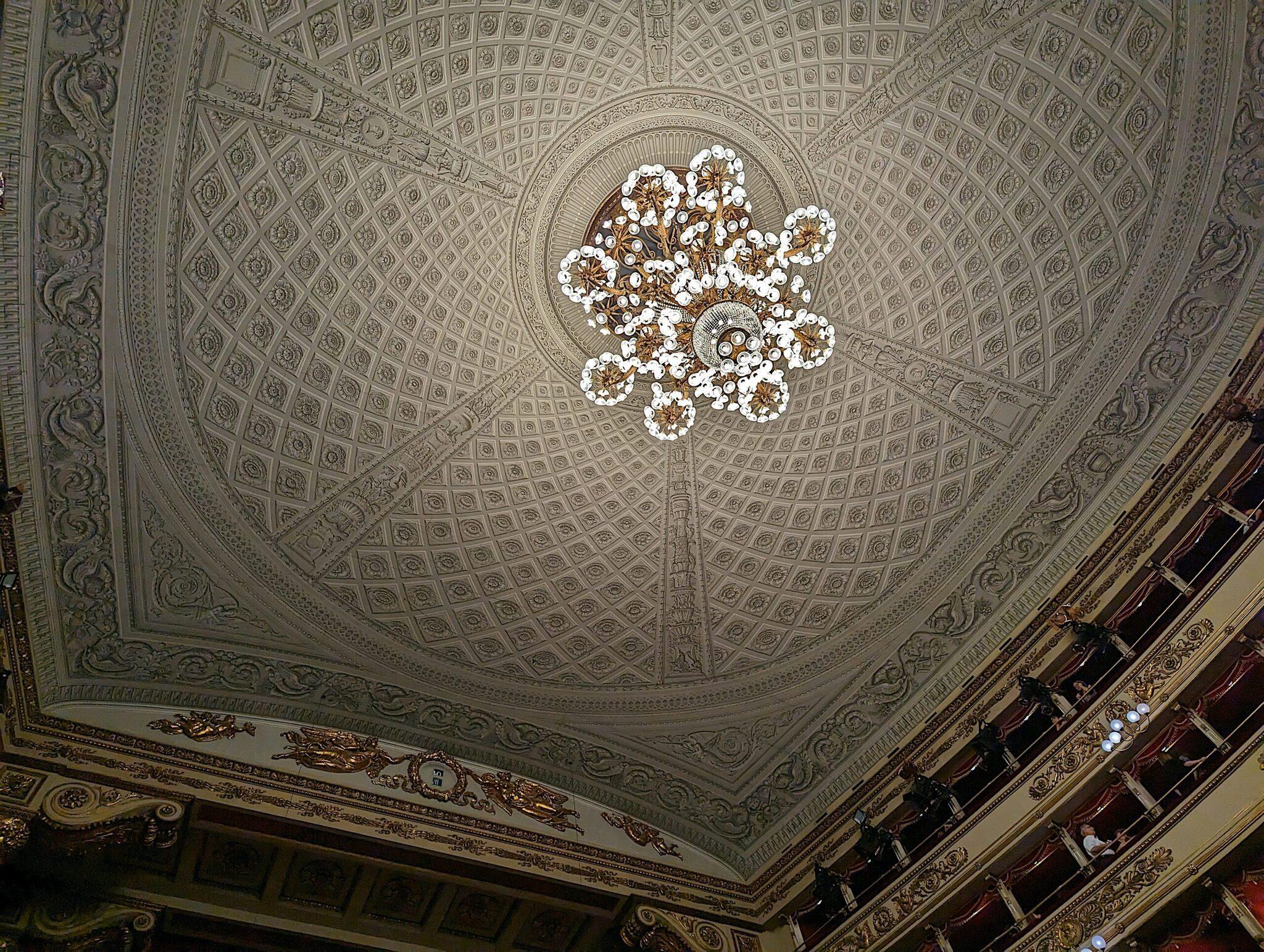 Plafond ornementé d’un théâtre avec lustre blanc et or, détails architecturaux élaborés et dorures