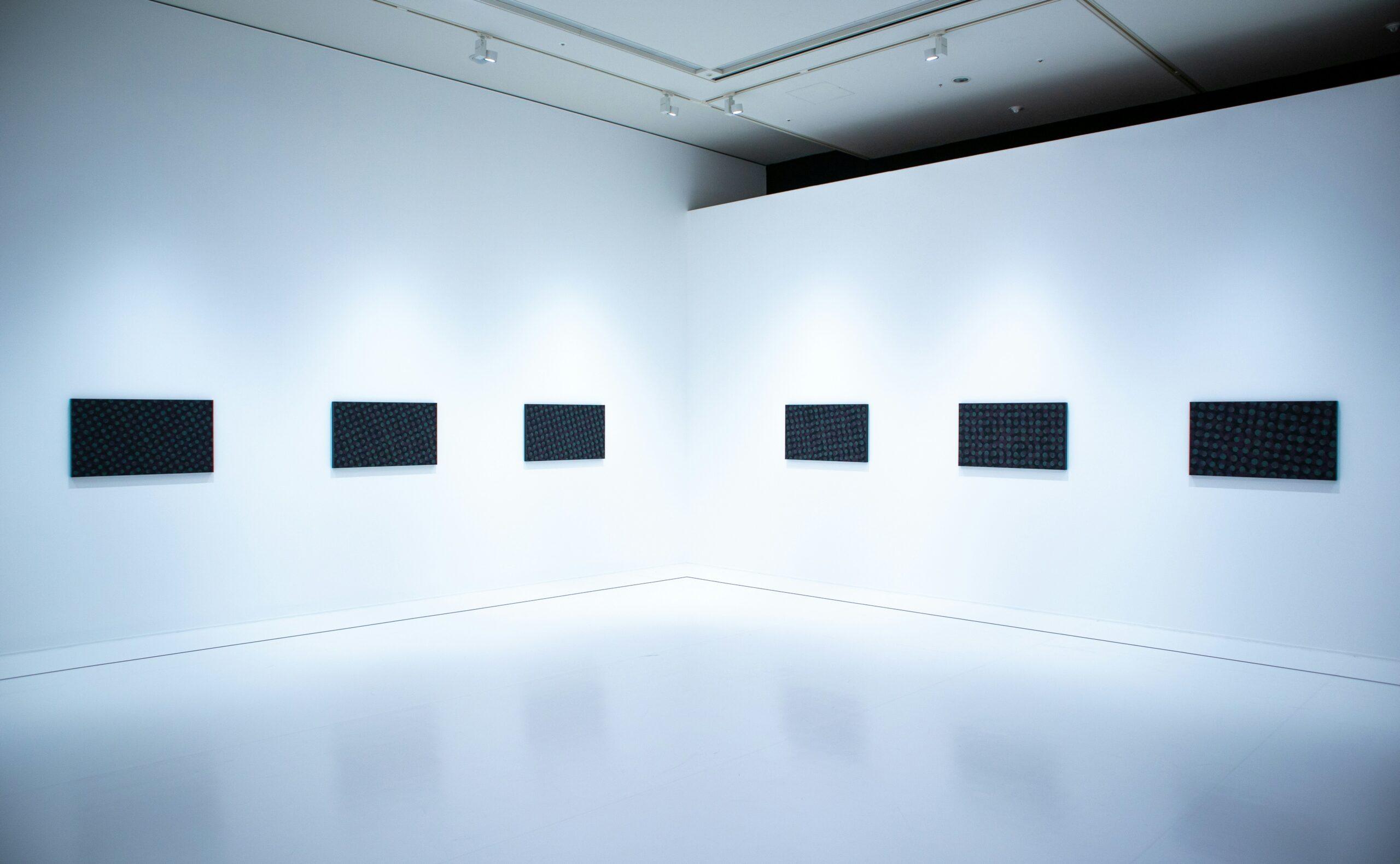 Une galerie d’art contemporain minimaliste avec six panneaux noirs disposés symétriquement sur mur blanc