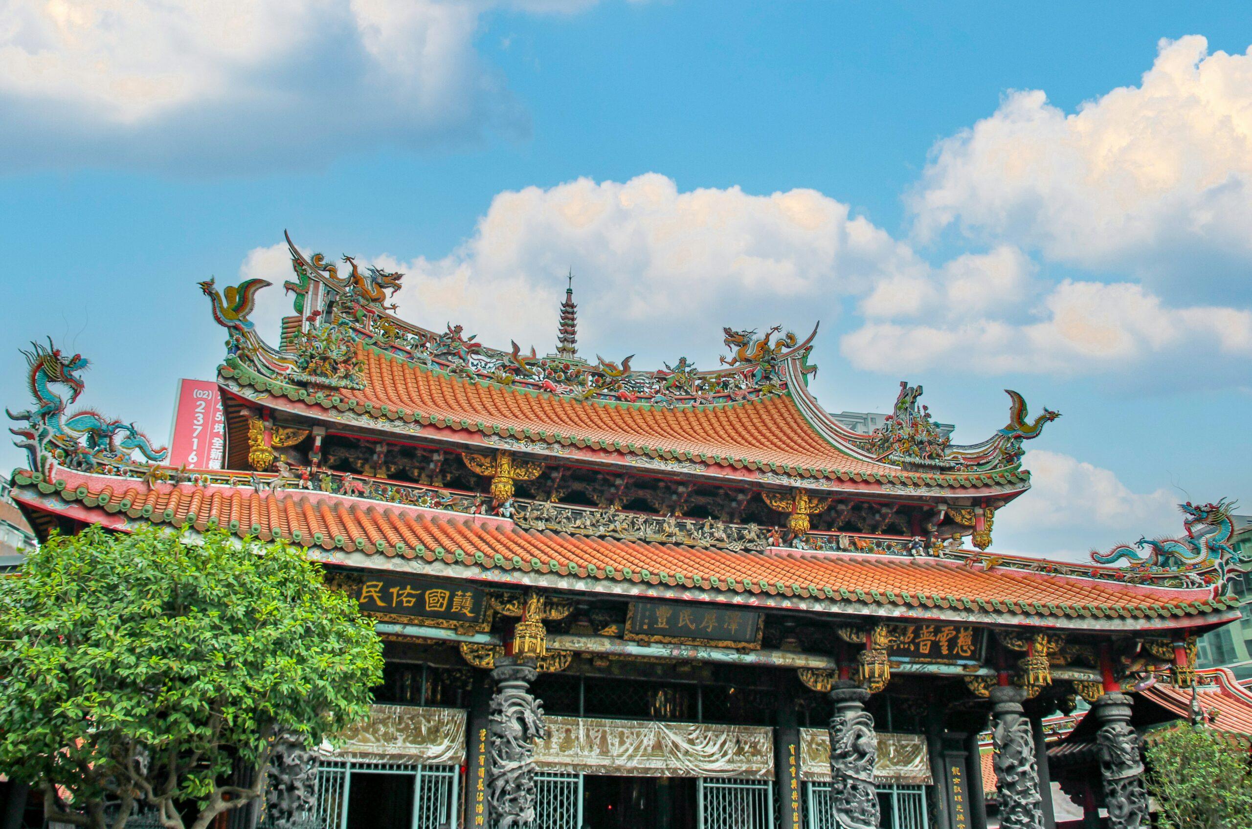 Temple bouddhiste asiatique aux toits ornementés orange et verts avec dragons colorés sous un ciel dégagé