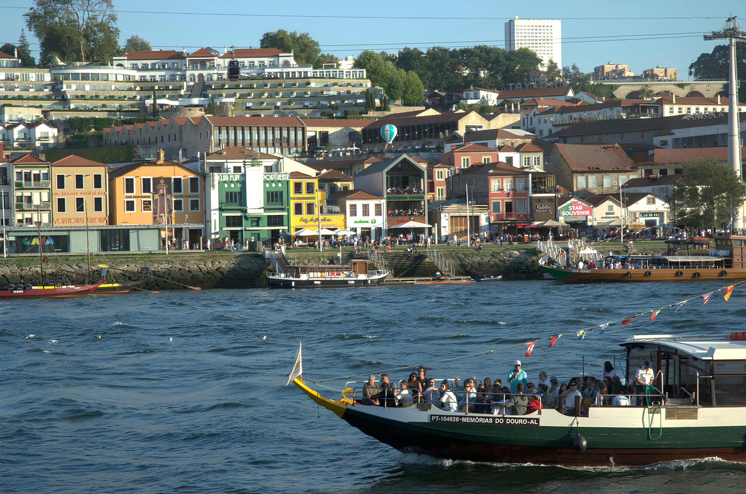 A colourful tourist boat on the river in front of picturesque waterfront facades and a lively riverside quay