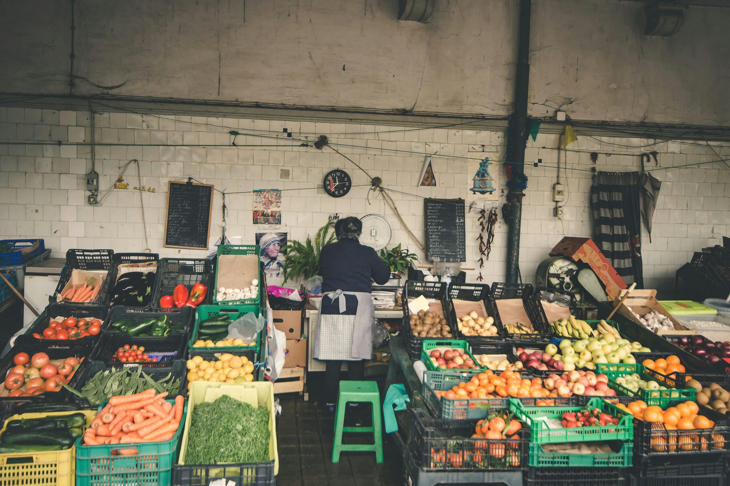 A fresh fruit and vegetable vendor in a traditional covered market, with colourful displays and white-tiled walls