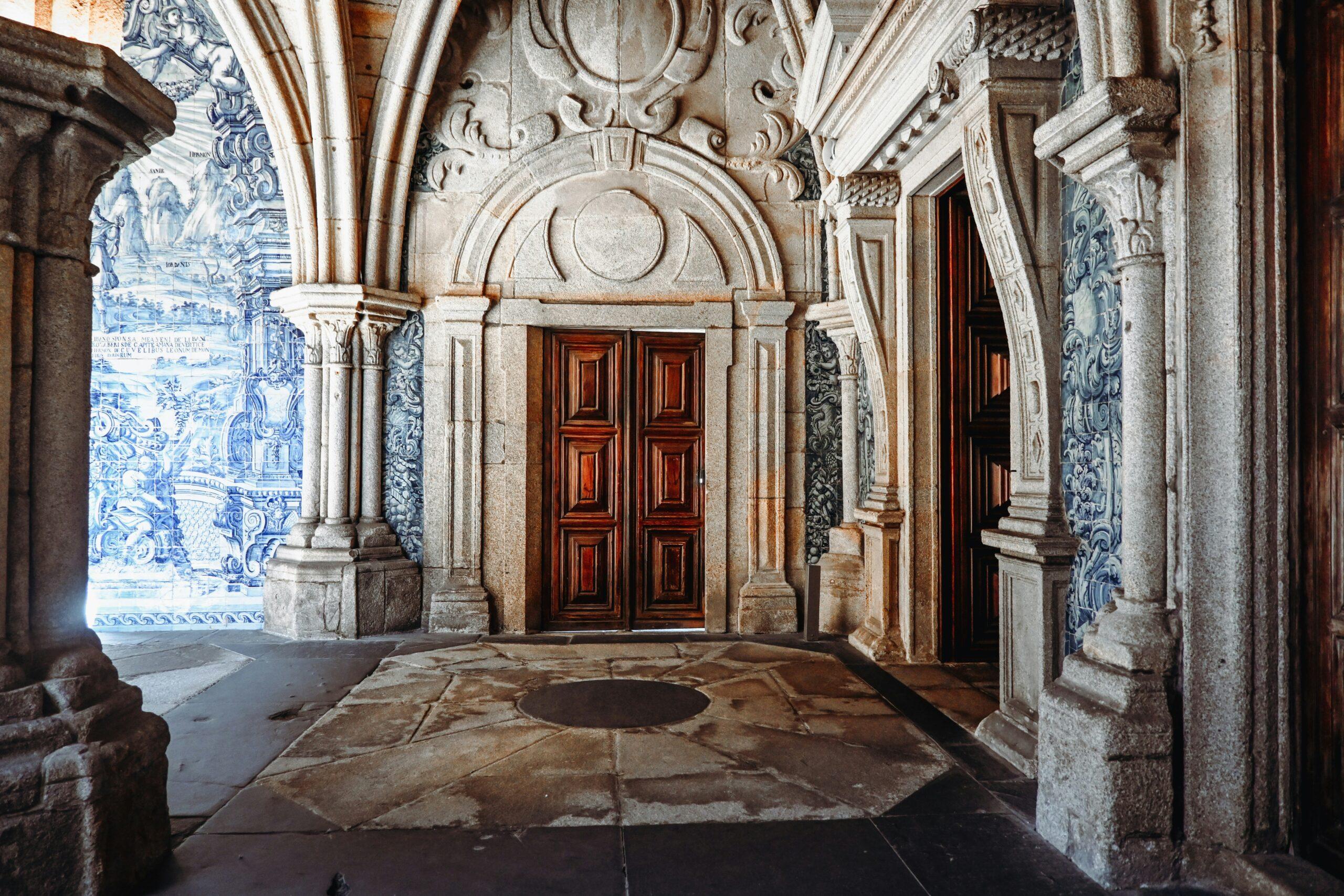 A baroque corridor decorated with blue Portuguese tiles and red wooden doors, flanked by carved stone columns