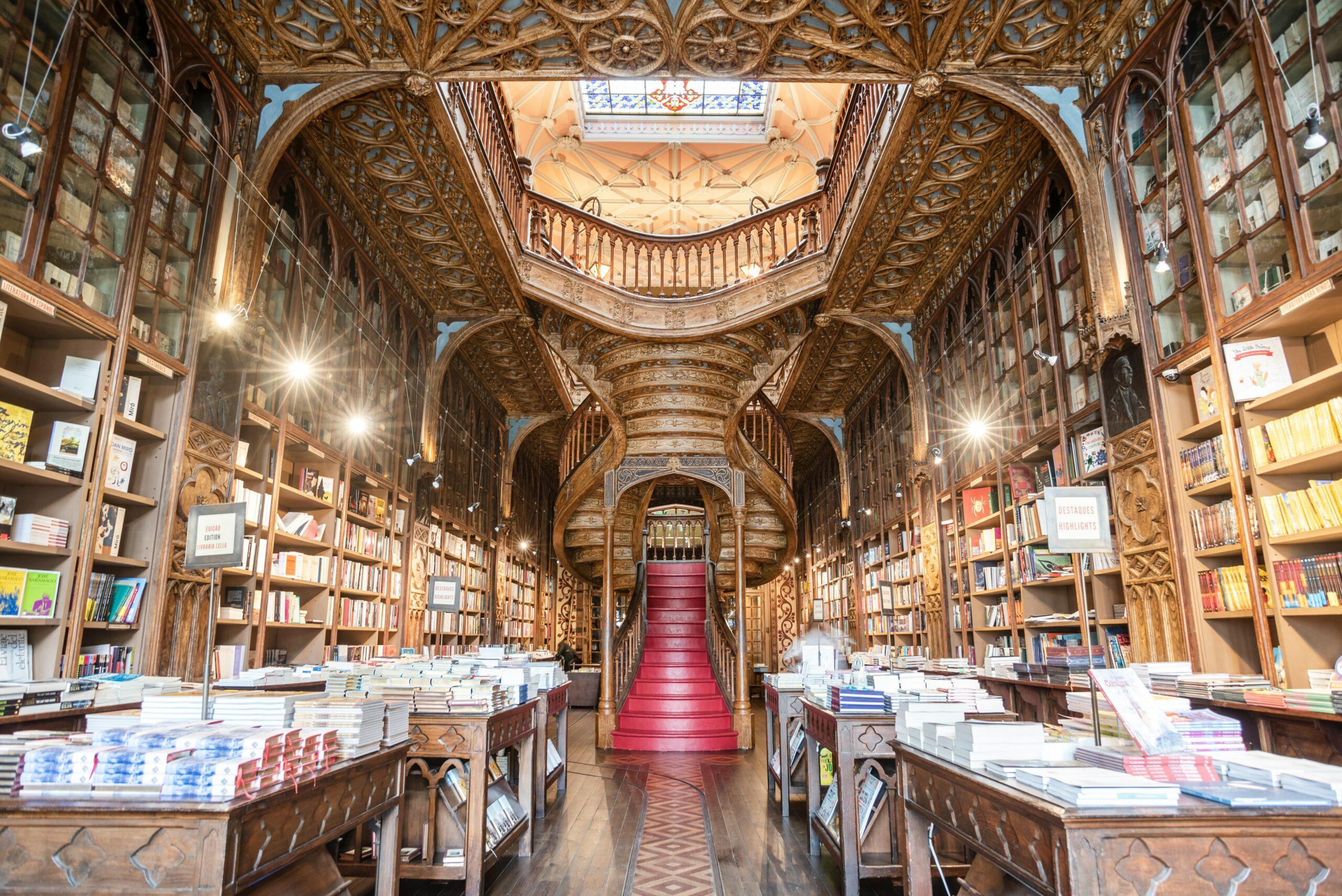 The ornate interior of a historic bookshop with a carved ceiling, wooden shelving and a sweeping red central staircase