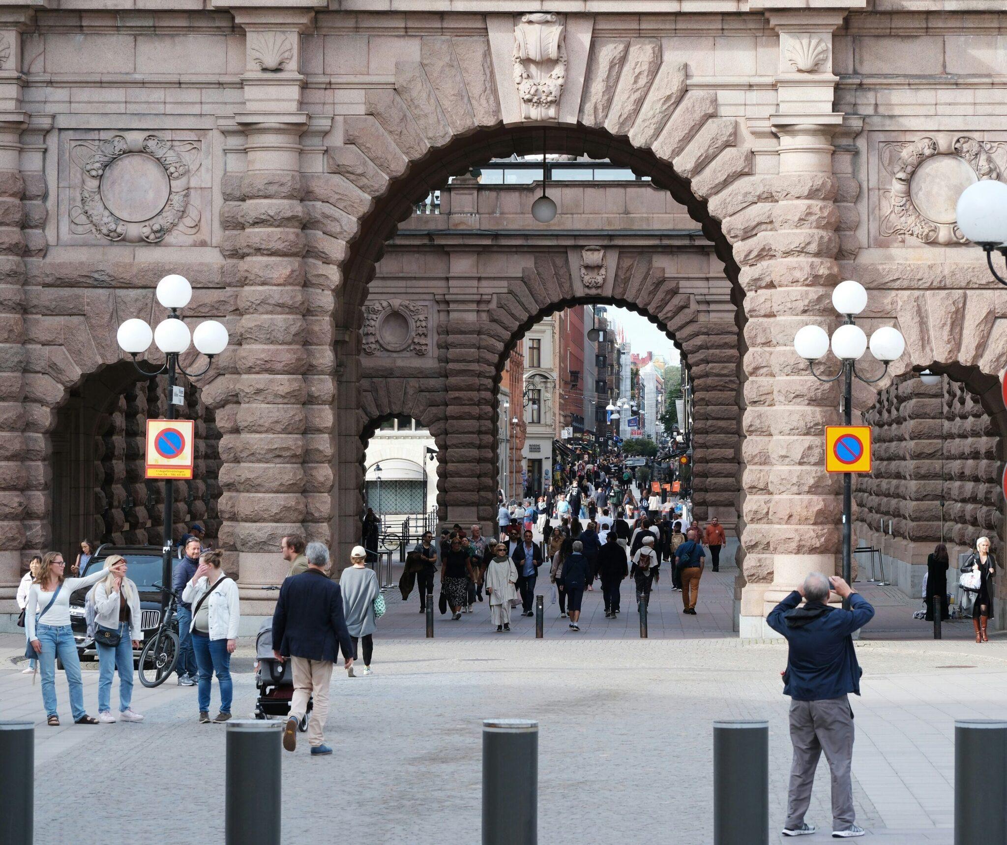 Una vivace strada pedonale che attraversa un imponente arco di pietra storico con edifici in mattoni sullo sfondo