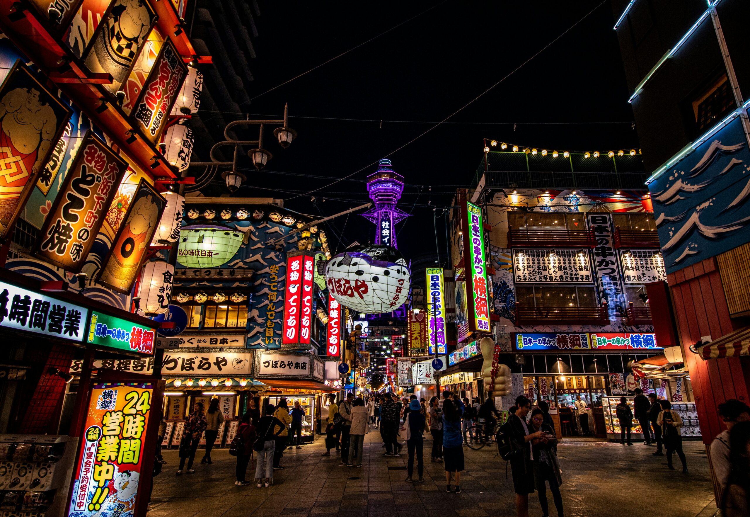 Une rue commerçante japonaise animée la nuit avec façades illuminées, enseignes colorées et architecture traditionnelle