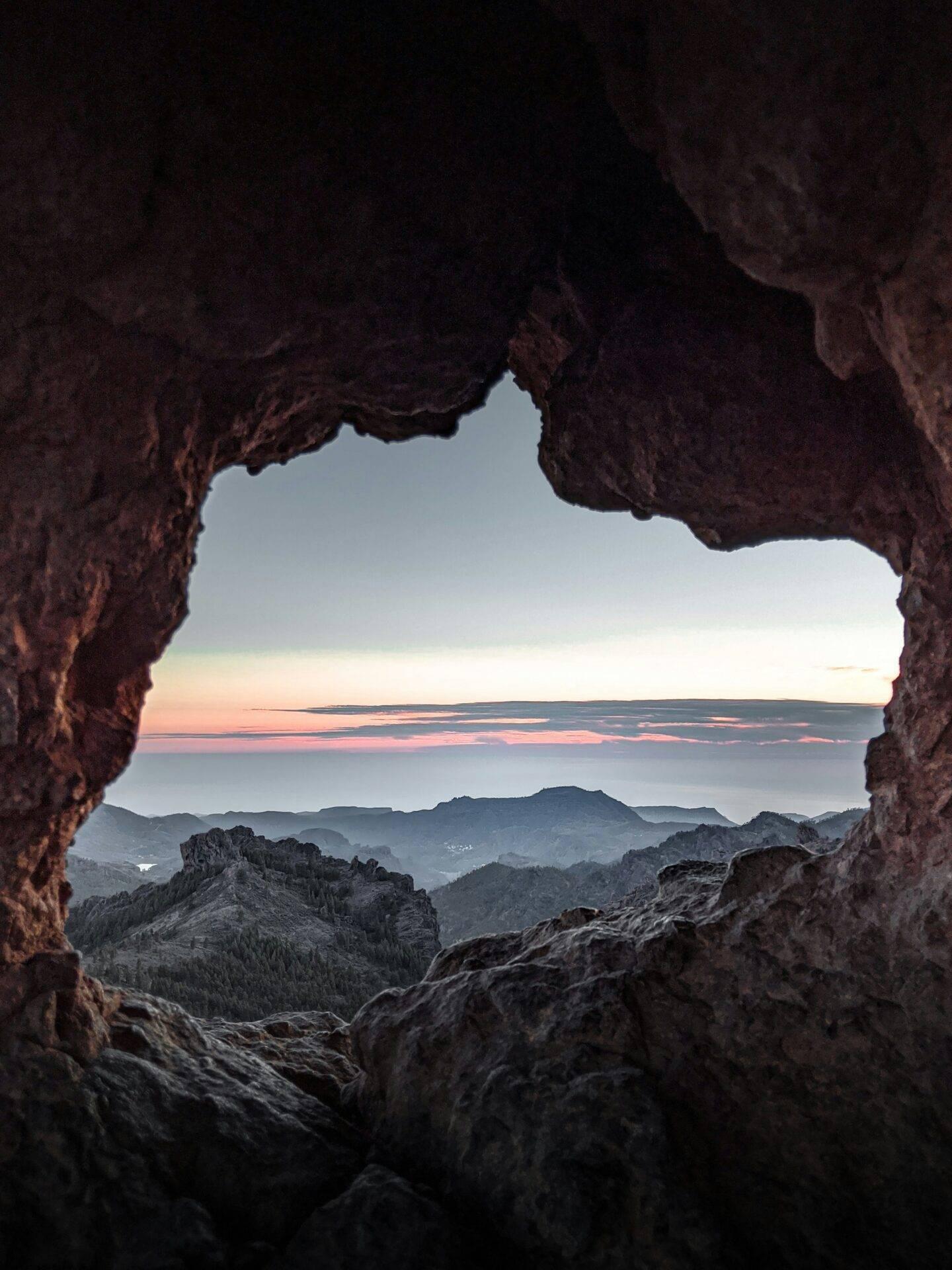 Vista da una grotta rocciosa su un paesaggio montano costiero al tramonto