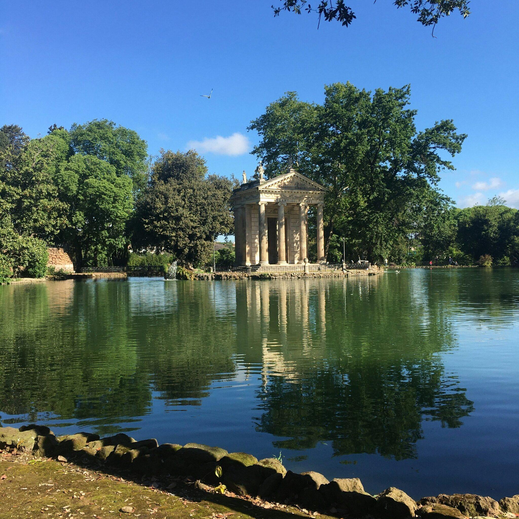 Temple classique à colonnes se reflétant dans un lac calme, entouré de verdure luxuriante par beau temps