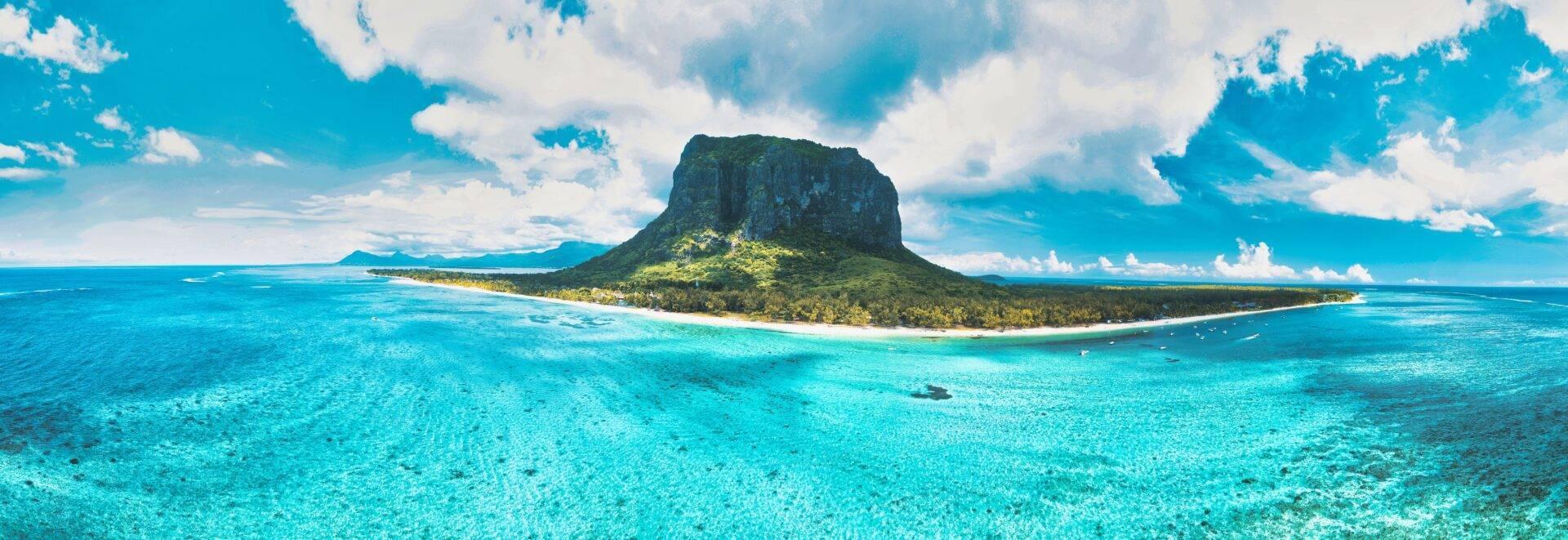 Eine tropische Insel mit grünen Steilklippen, umgeben von kristallklarem türkisem Wasser unter leicht bewölktem Himmel