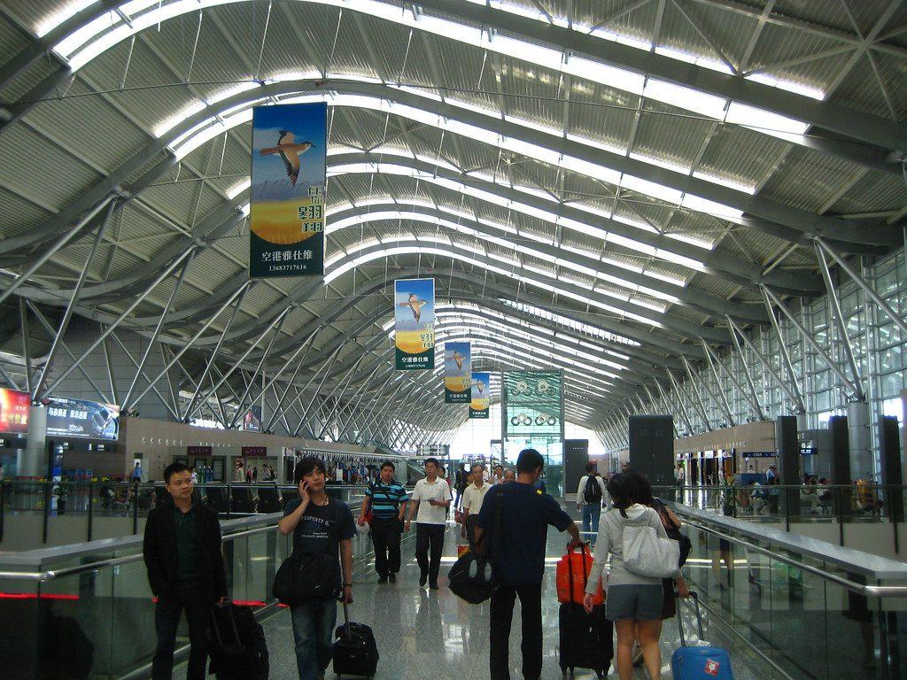 Voyageurs attendant dans un terminal d’aéroport face aux tableaux de départ affichant des retards