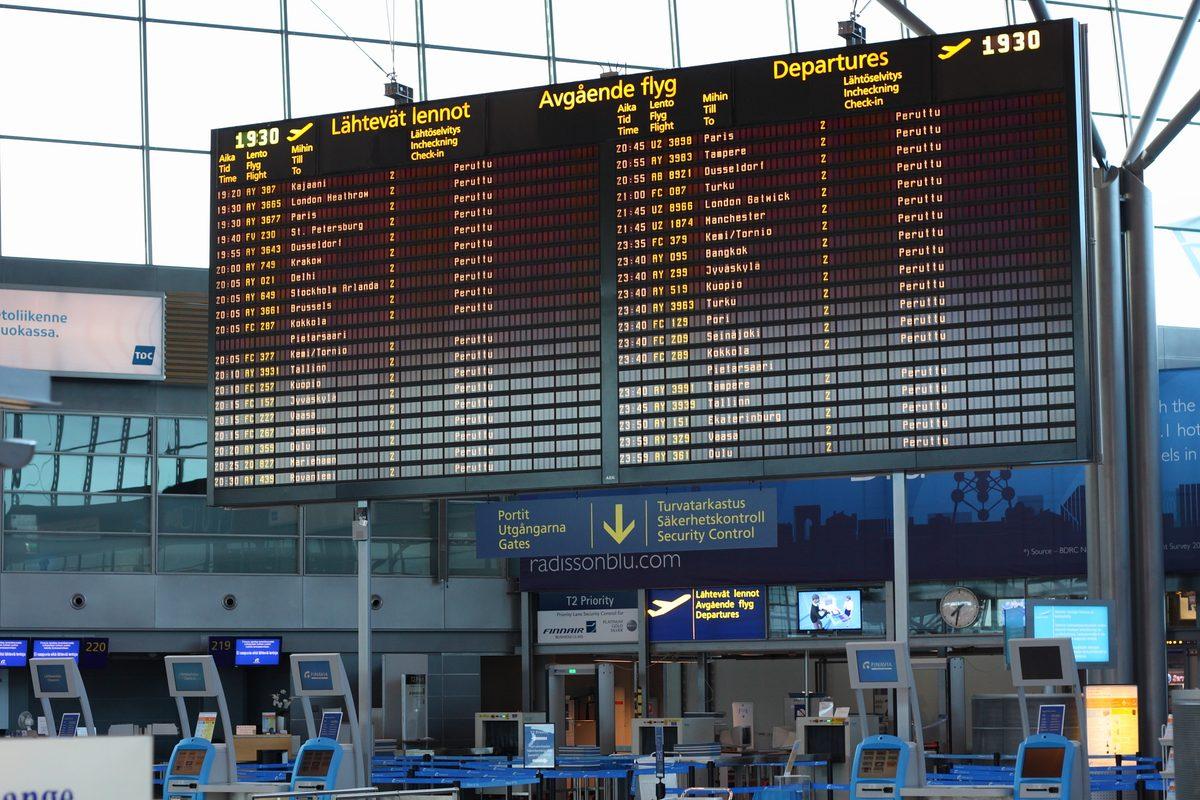 Passager consultant son téléphone devant un tableau d’affichage de vols annulés dans un aéroport