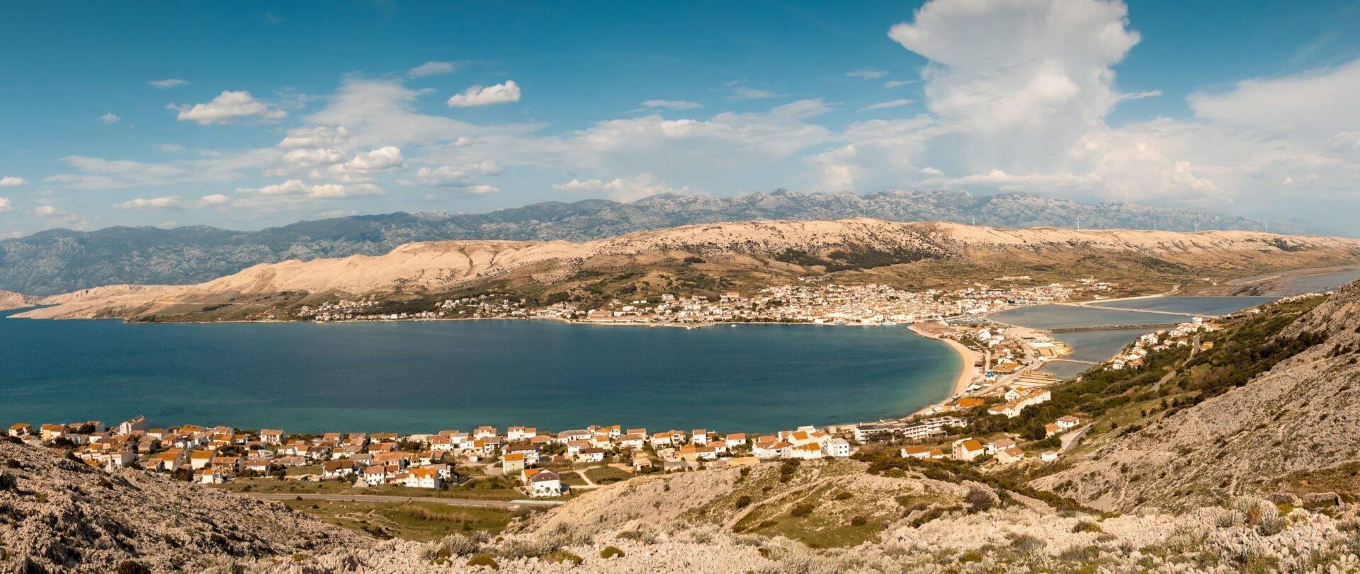 Panoramaansicht einer mediterranen Bucht mit weißen Küstendörfern und felsigem Gebirgsmassiv im Hintergrund