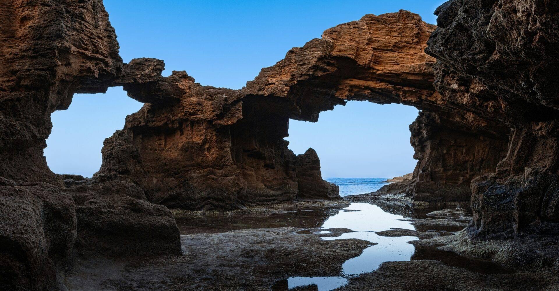 Stone ruins with natural arches overlooking a rocky beach and reflective rock pools