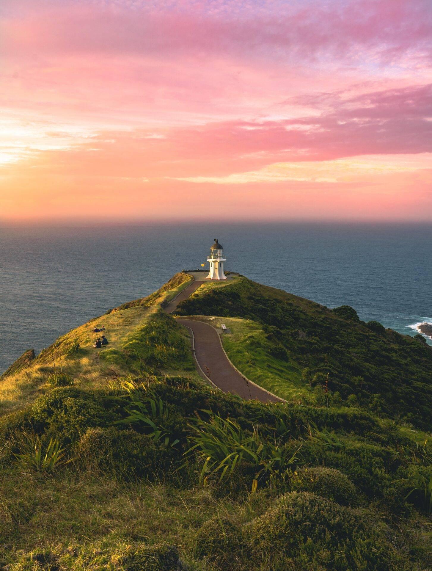 Un phare blanc sur une falaise verdoyante surplombant l’océan au coucher du soleil