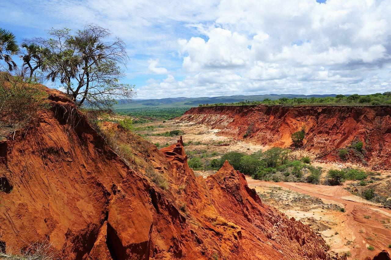 Carrière de latérite avec formations rocheuses rouges dominant une vallée verdoyante sous ciel nuageux