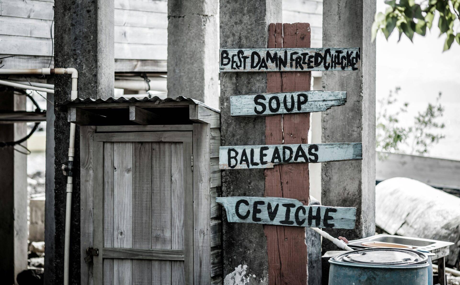 Panneau en bois peint indiquant des plats locaux (soupe, baleadas, ceviche) devant une porte rustique