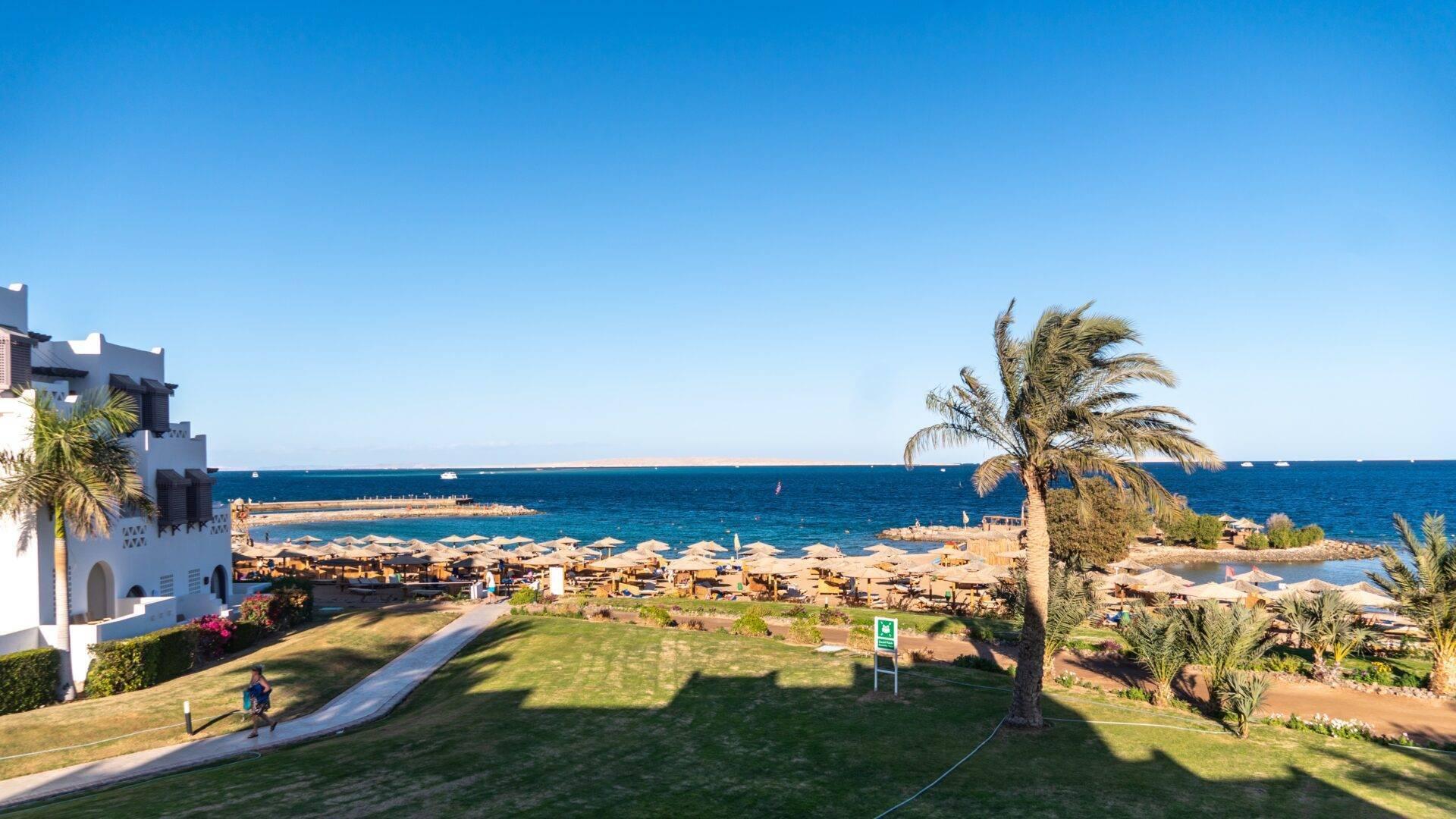 Vue aérienne d’une station balnéaire avec plage de sable, palmiers et architecture blanche face à la mer turquoise
