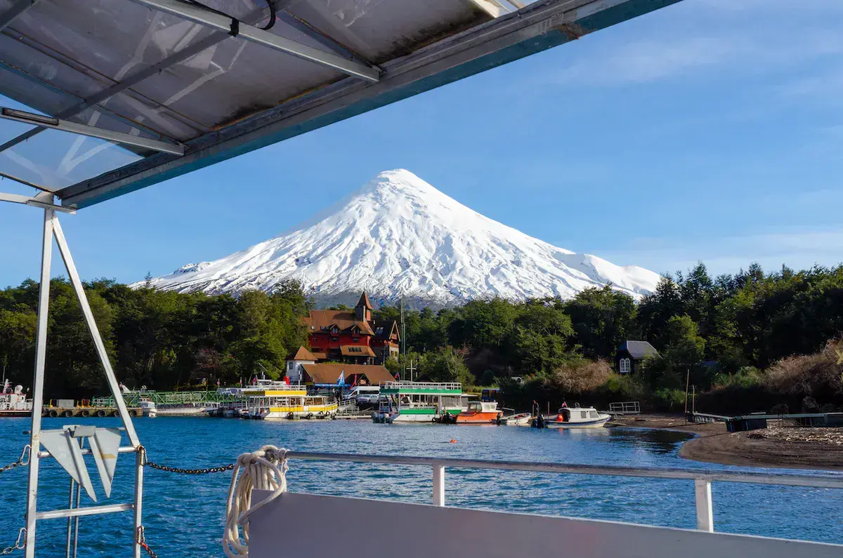 Vue depuis un bateau sur un lac avec un volcan enneigé majestueux en arrière-plan et un château coloré sur la rive