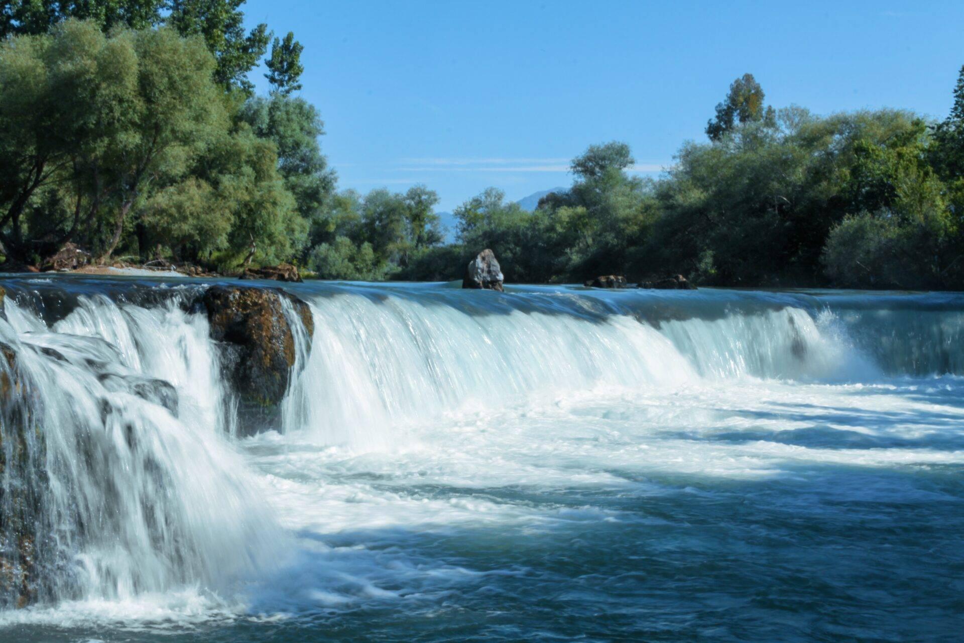 Une cascade spectaculaire s’écoule dans une rivière turquoise entourée de végétation luxuriante et de montagnes