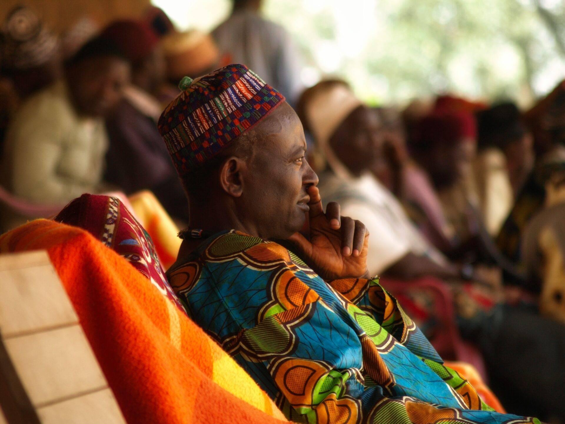 Un homme vêtu de tissus traditionnels colorés assiste à une cérémonie culturelle africaine en compagnie d’autres participants