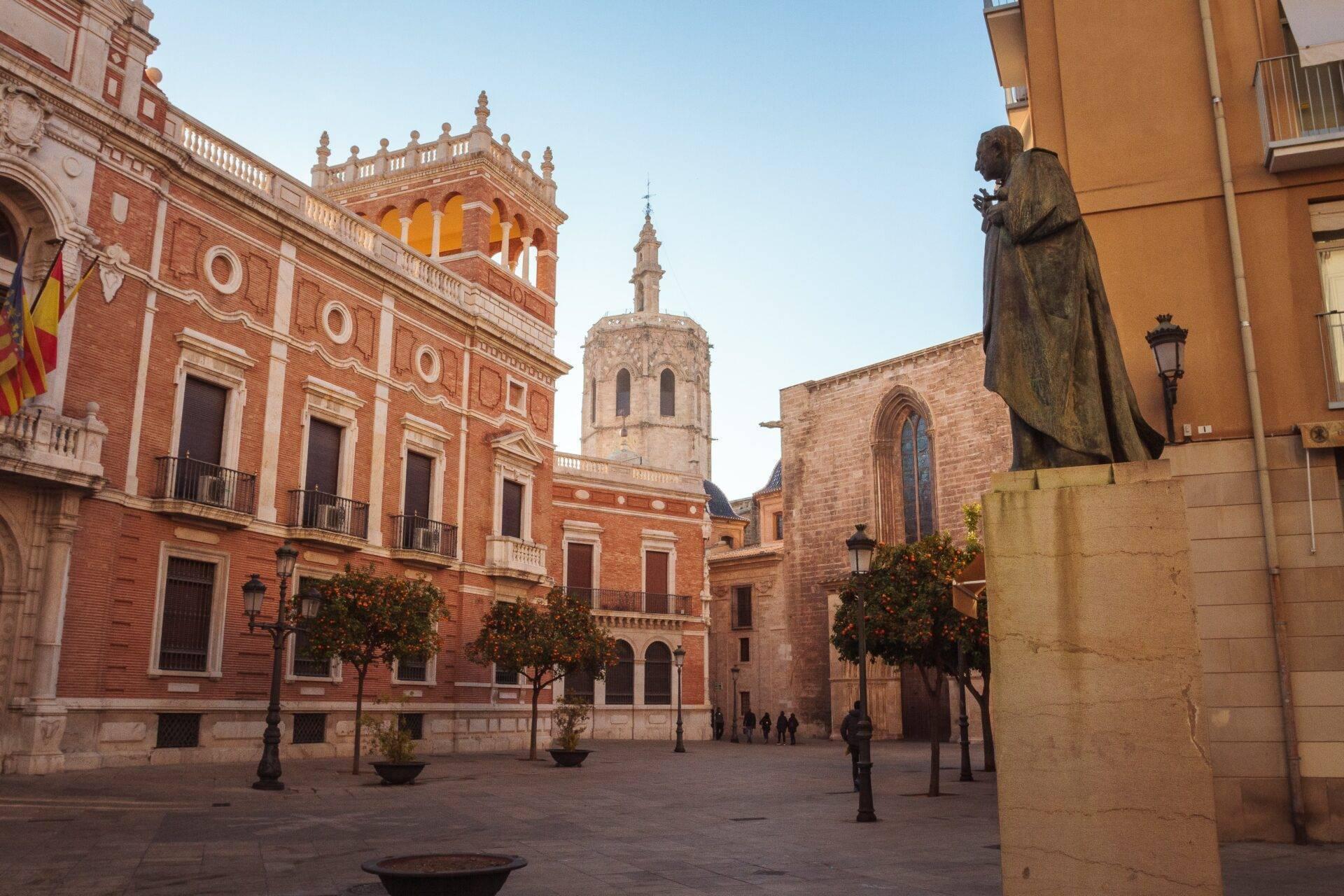 Une place historique en Espagne avec bâtiments en brique rouge, église et statue monumentale sous un ciel clair