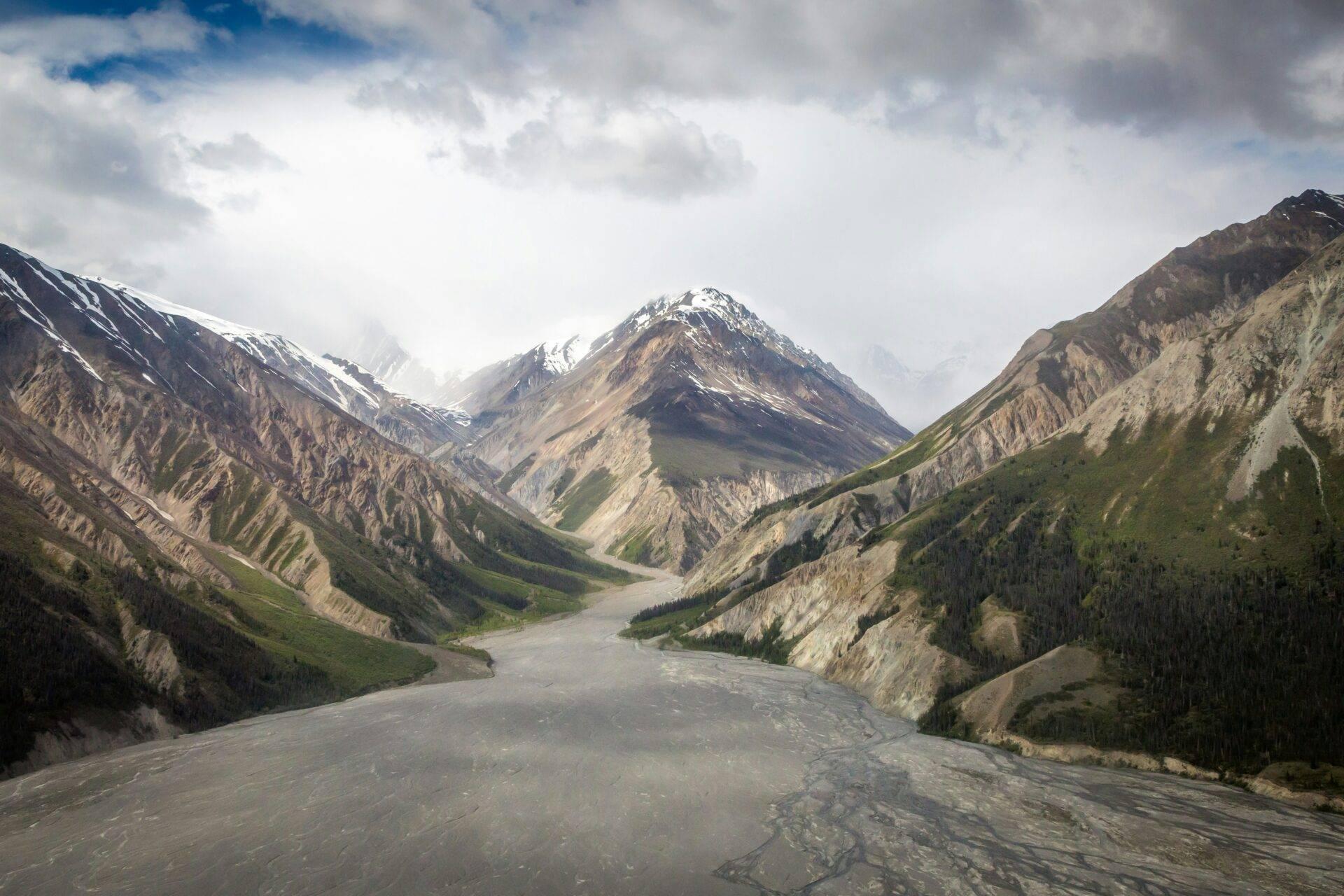 Une vallée alpine glacée traversée par un fleuve gris, encadrée de montagnes enneigées et de forêts de conifères