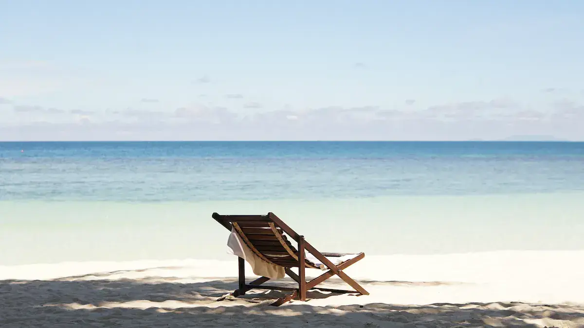 Une chaise longue en bois face à la mer turquoise sur une plage de sable blanc déserte