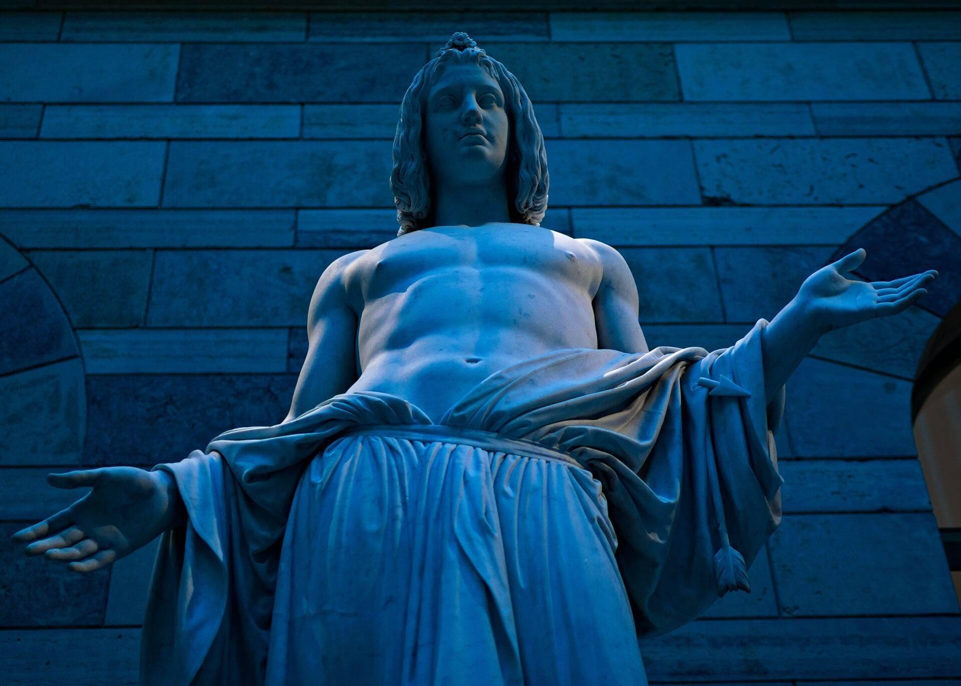 Statue de marbre en éclairage bleu nocturne contre un mur de pierre, posture contemplative avec drapé classique