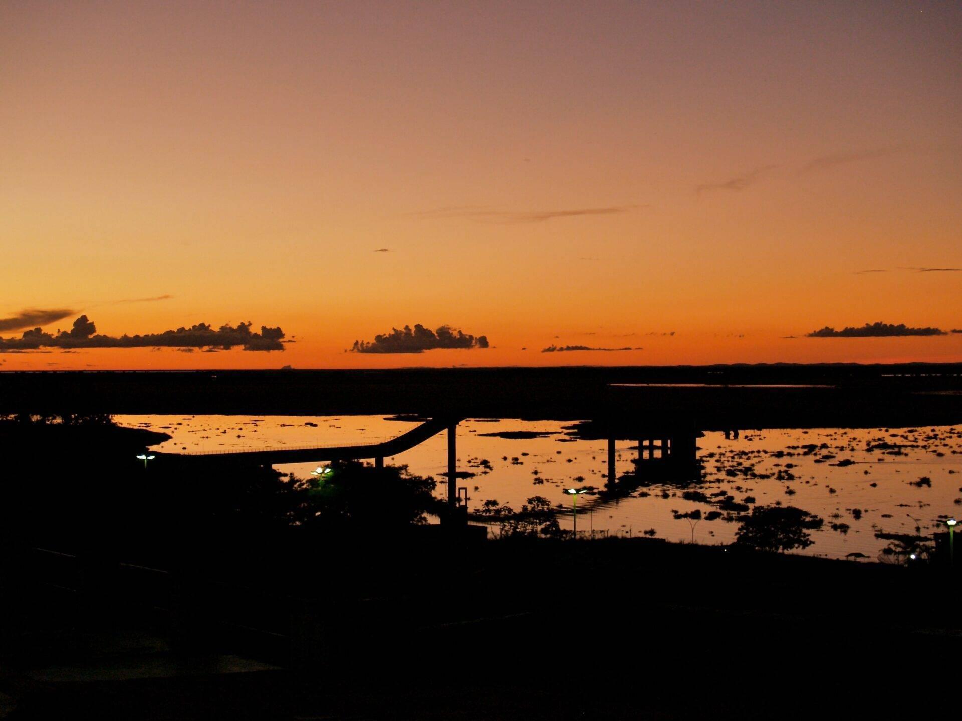 Coucher de soleil doré sur un fleuve avec pont routier et zones inondées en silhouette