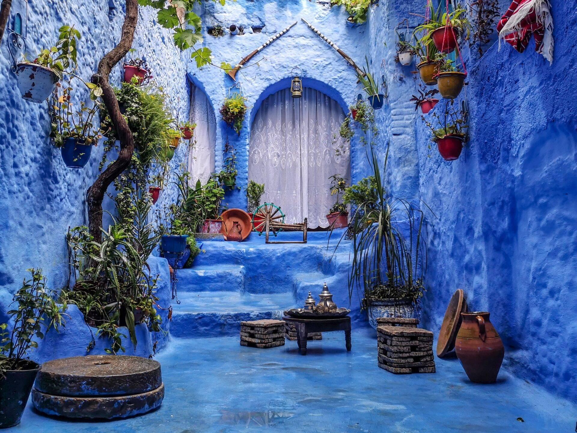 Cour intérieure bleue avec porte arrondie, plantes en pots et mobilier traditionnel marocain