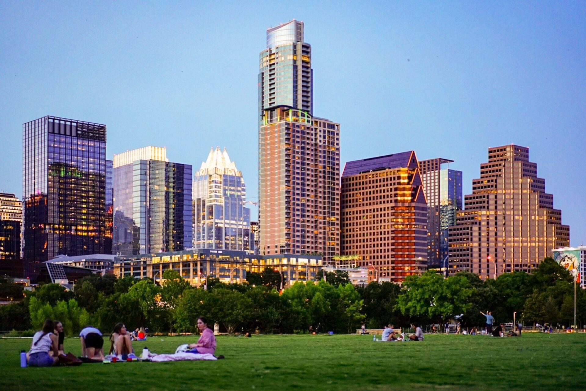 Skyline urbain avec gratte-ciel modernes et parc verdoyant au premier plan où des visiteurs se détendent