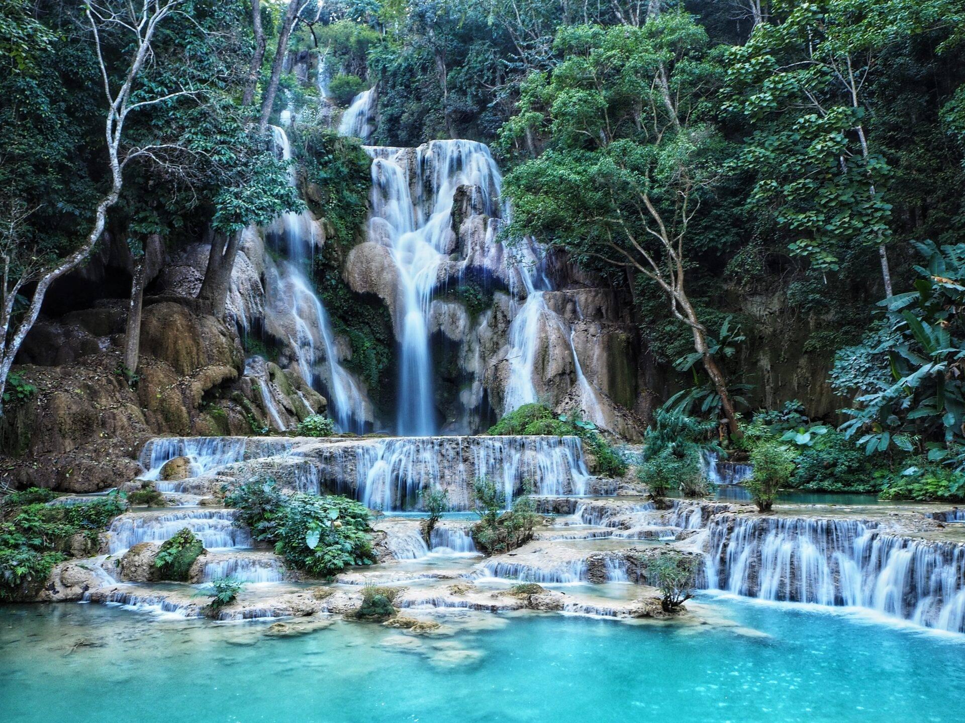 Une cascade à étages turquoise en cascade dans une forêt tropicale luxuriante entourée de roches et de végétation