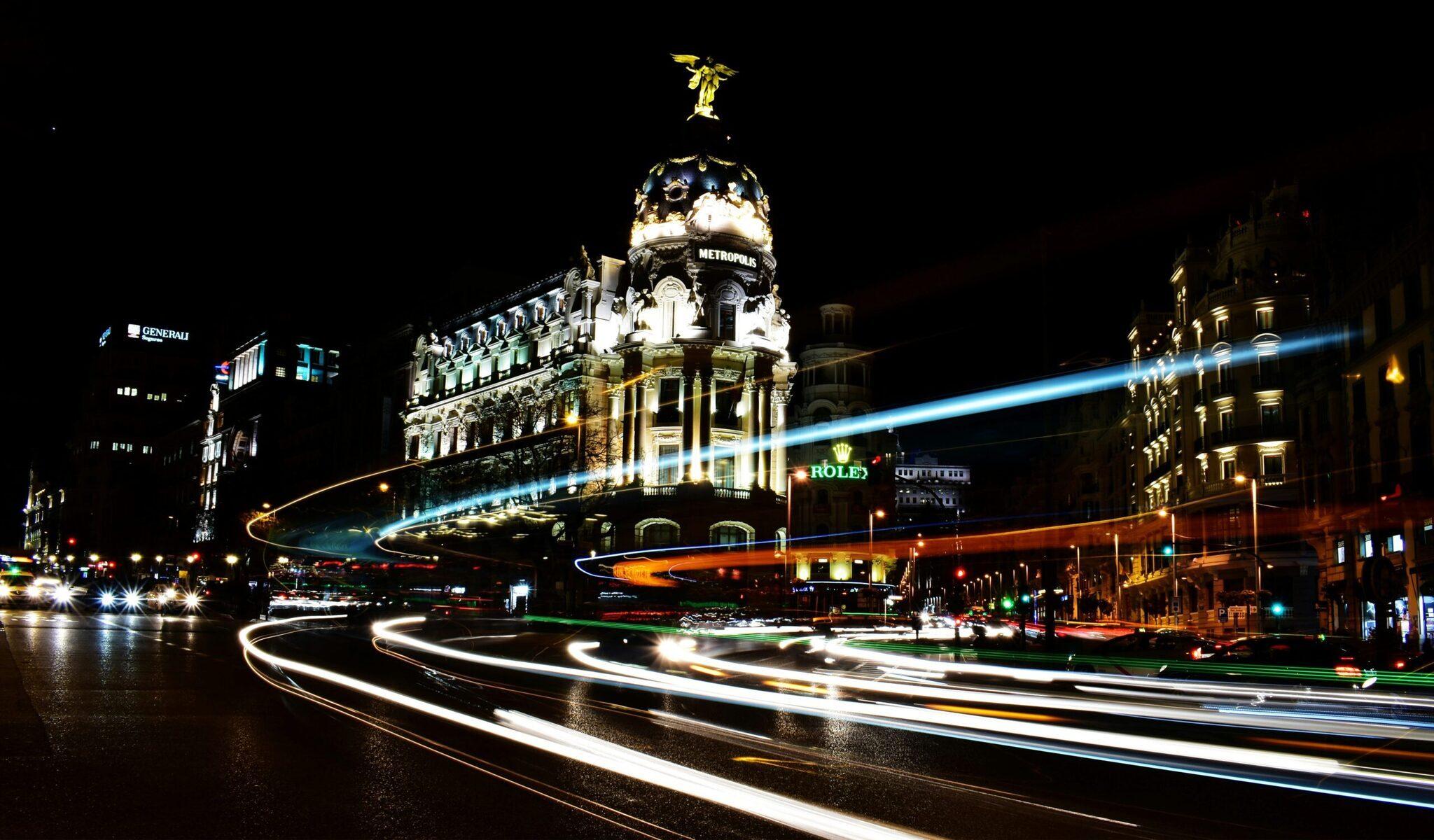 Vue nocturne d’une place urbaine européenne avec un bâtiment emblématique illuminé et traînées lumineuses de circulation automobile