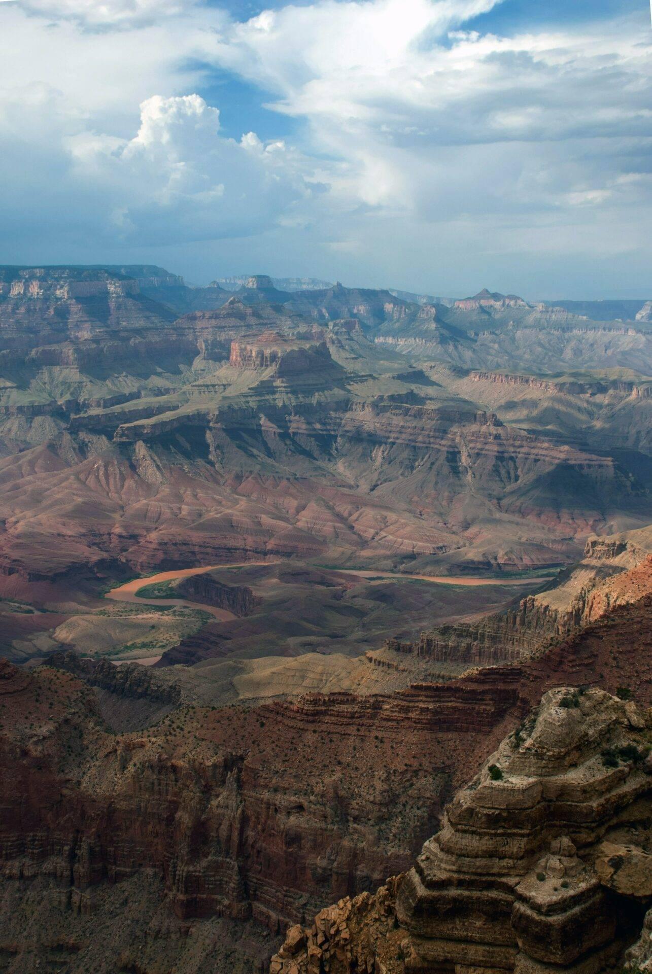 Vue aérienne d’un immense canyon aux falaises stratifiées rouges et brunes, avec une rivière sinueuse au fond