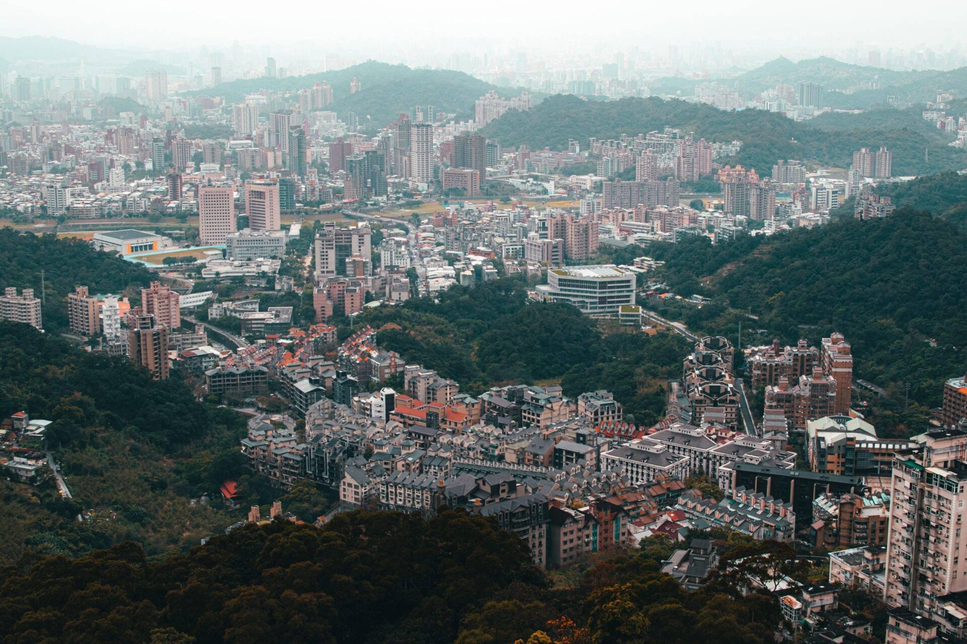 Vue aérienne d’une ville montagneuse dense avec immeubles résidentiels, verdure environnante et brume atmosphérique