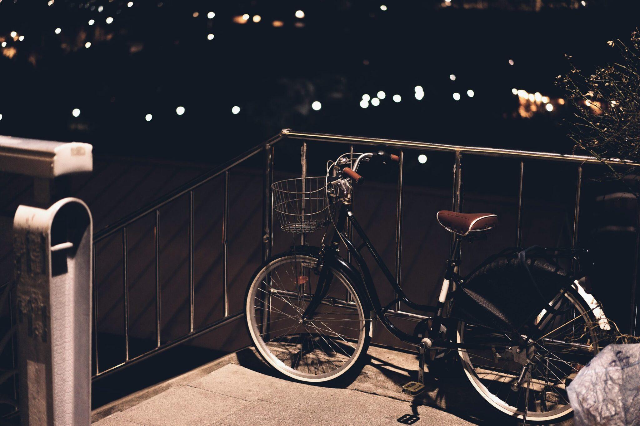 Deux vélos stationnés contre une barrière métallique la nuit avec lumières de ville en arrière-plan