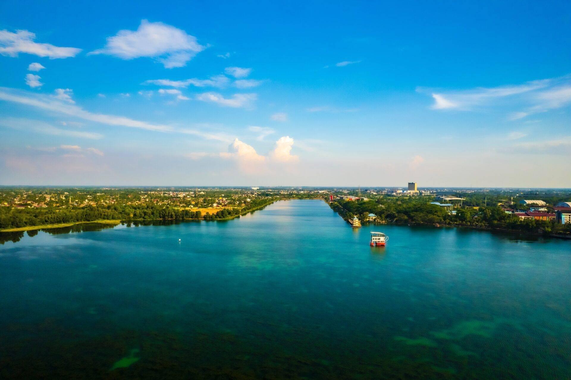 Vue aérienne d’un fleuve turquoise bordé de végétation tropicale avec un bateau touristique et une ville côtière