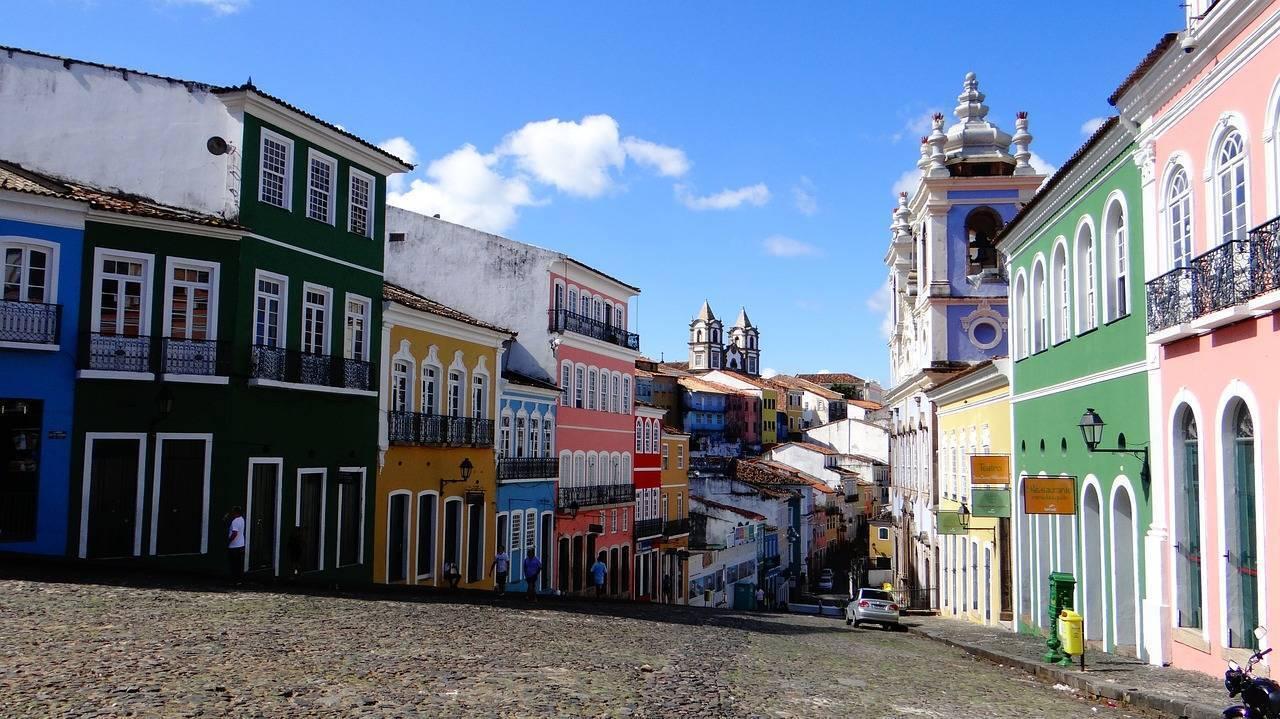 Une rue pavée historique bordée de maisons colorées avec églises coloniales en arrière-plan sous un ciel bleu