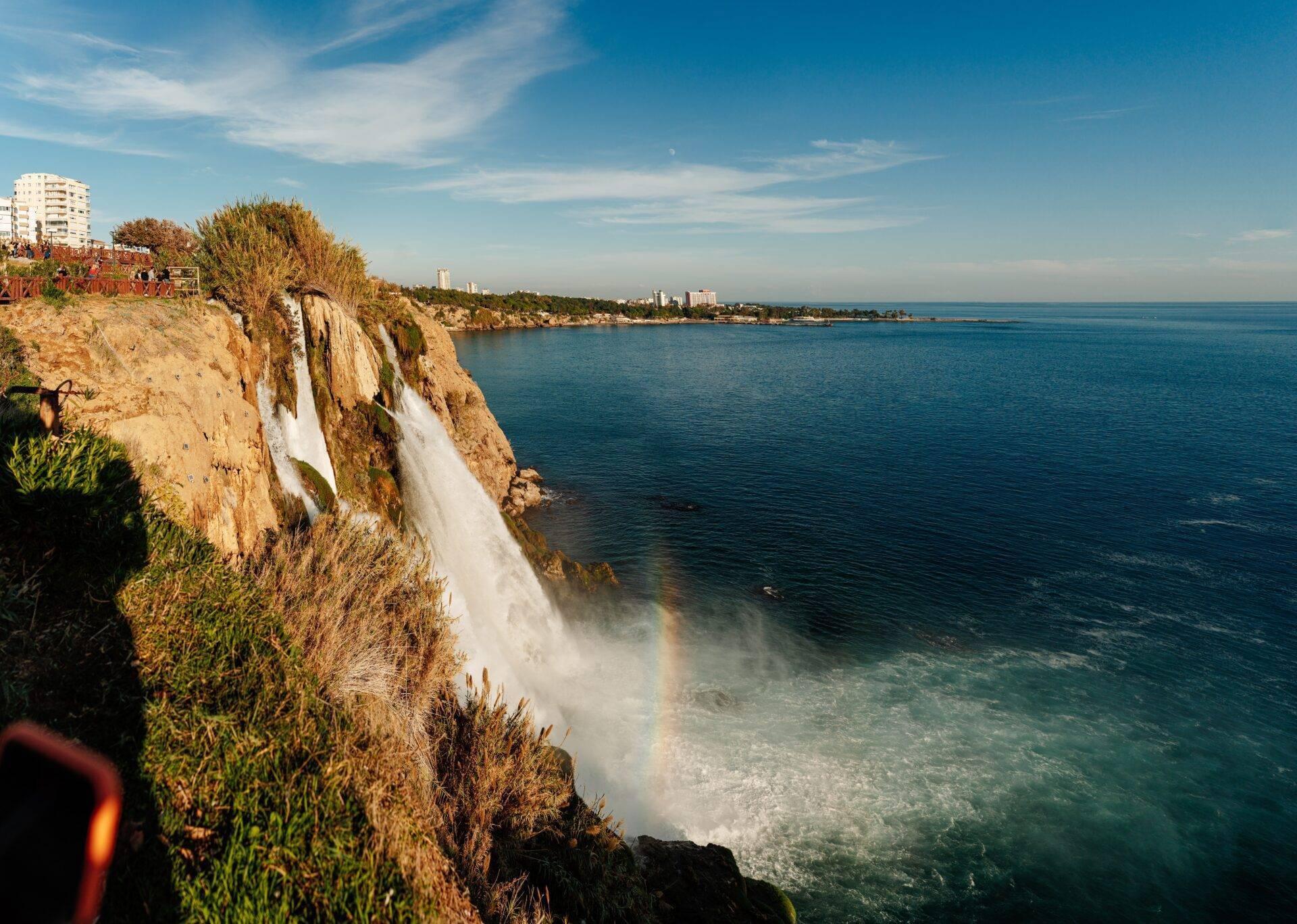 Cascade spectaculaire dégringolant d’une falaise côtière rocheuse vers la mer turquoise méditerranéenne sous un ciel bleu dégagé