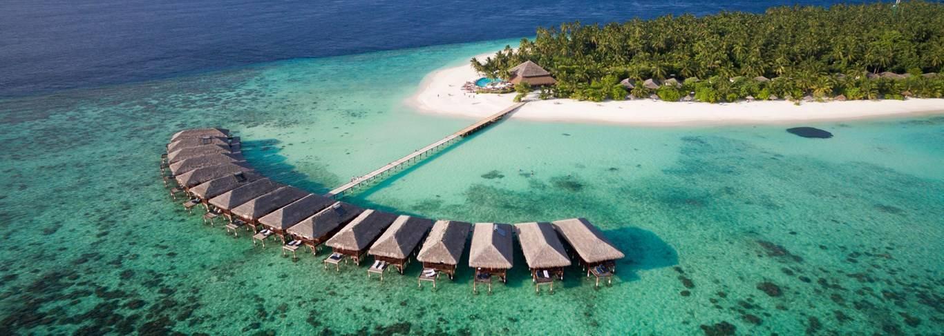 Vue aérienne d’un resort tropical avec bungalows sur pilotis, plage blanche et lagon turquoise aux Maldives