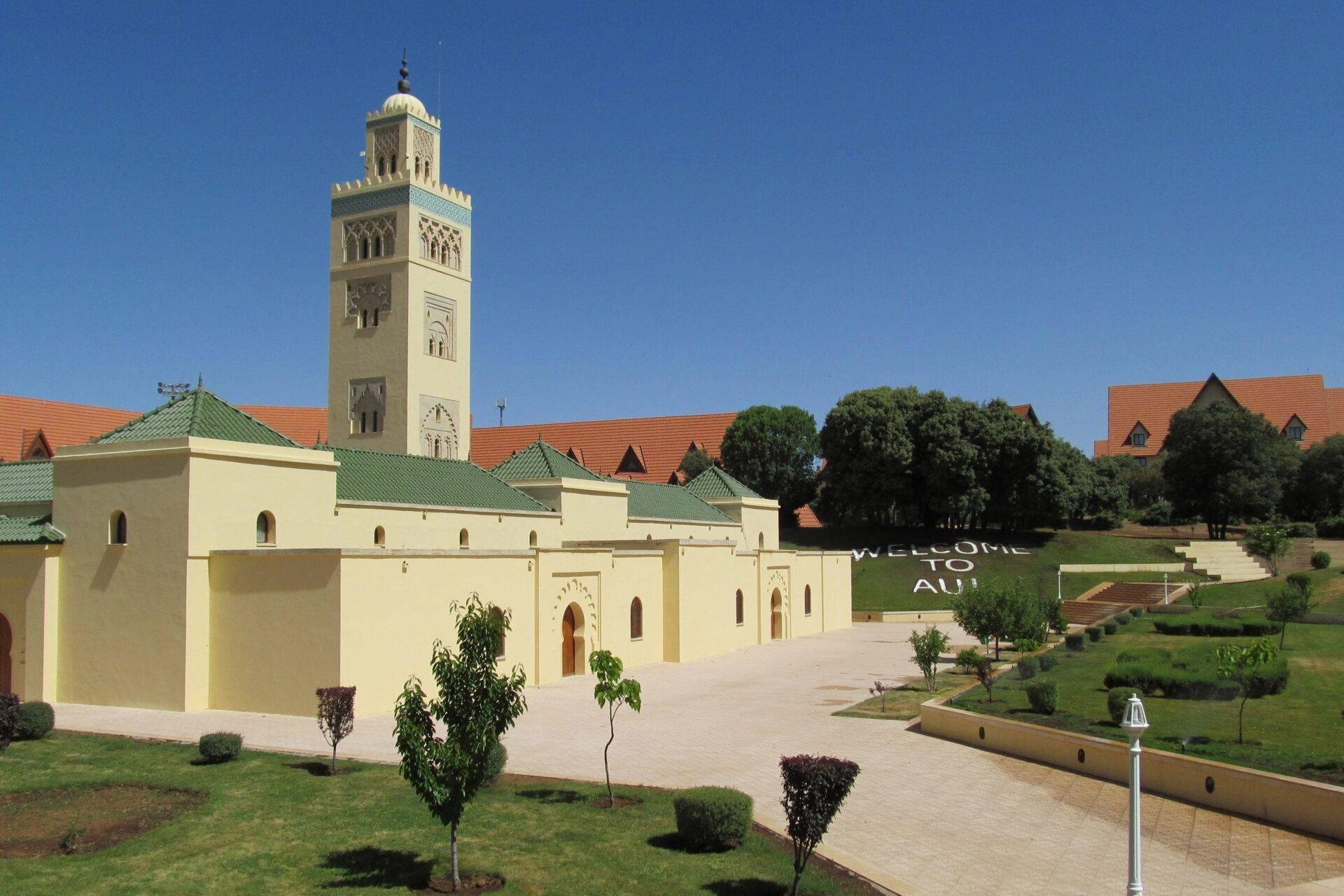 Une mosquée marocaine moderne avec minaret élancé, cour pavée et bâtiments aux toits orange sous ciel bleu