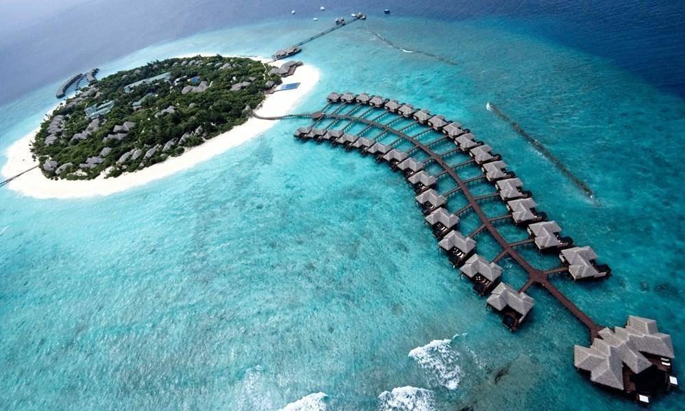 Vue aérienne d’un resort tropical avec bungalows sur pilotis, île verdoyante et lagon turquoise aux Maldives
