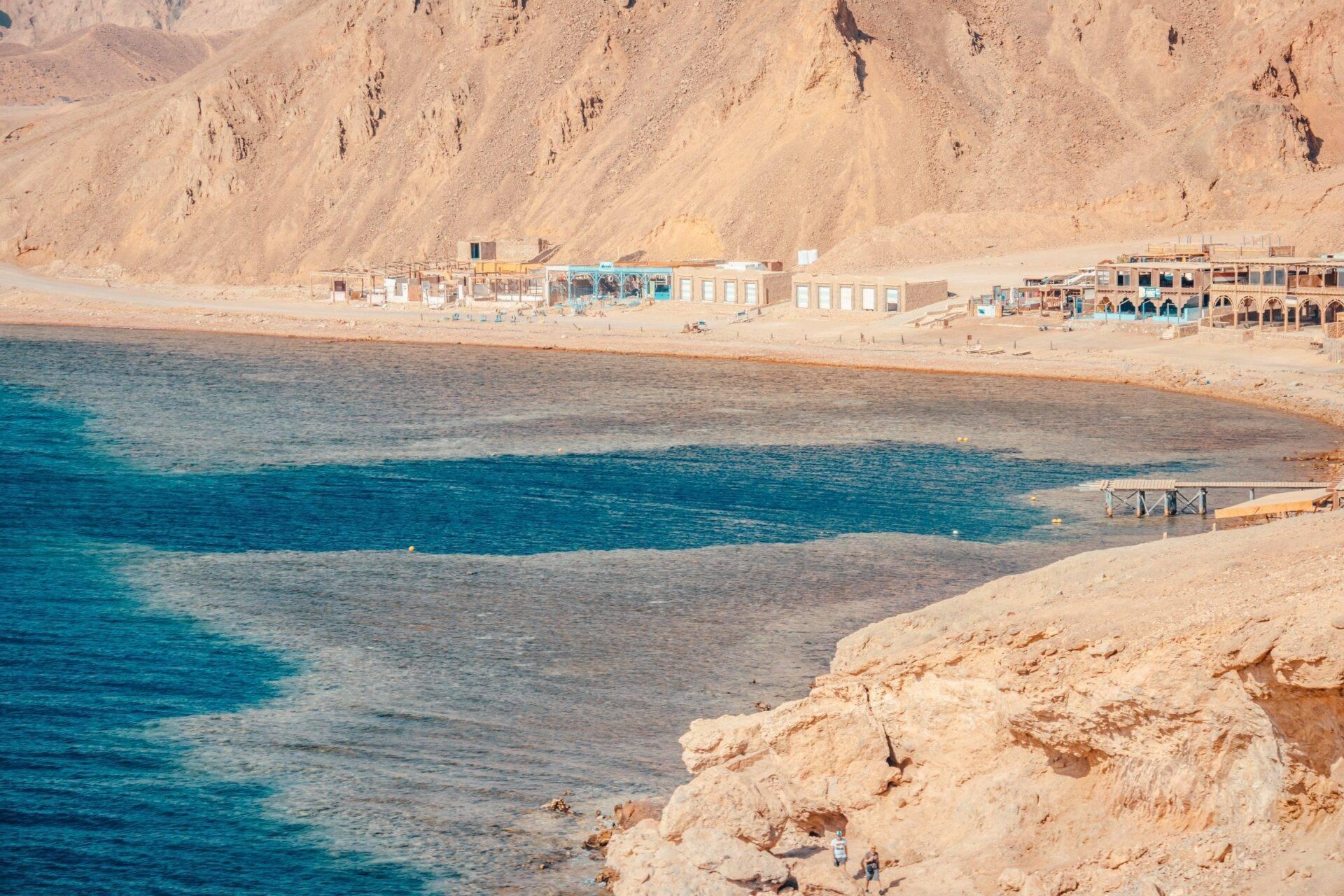 Une plage déserte en Égypte avec des bâtiments côtiers, des montagnes arides et une mer turquoise cristalline