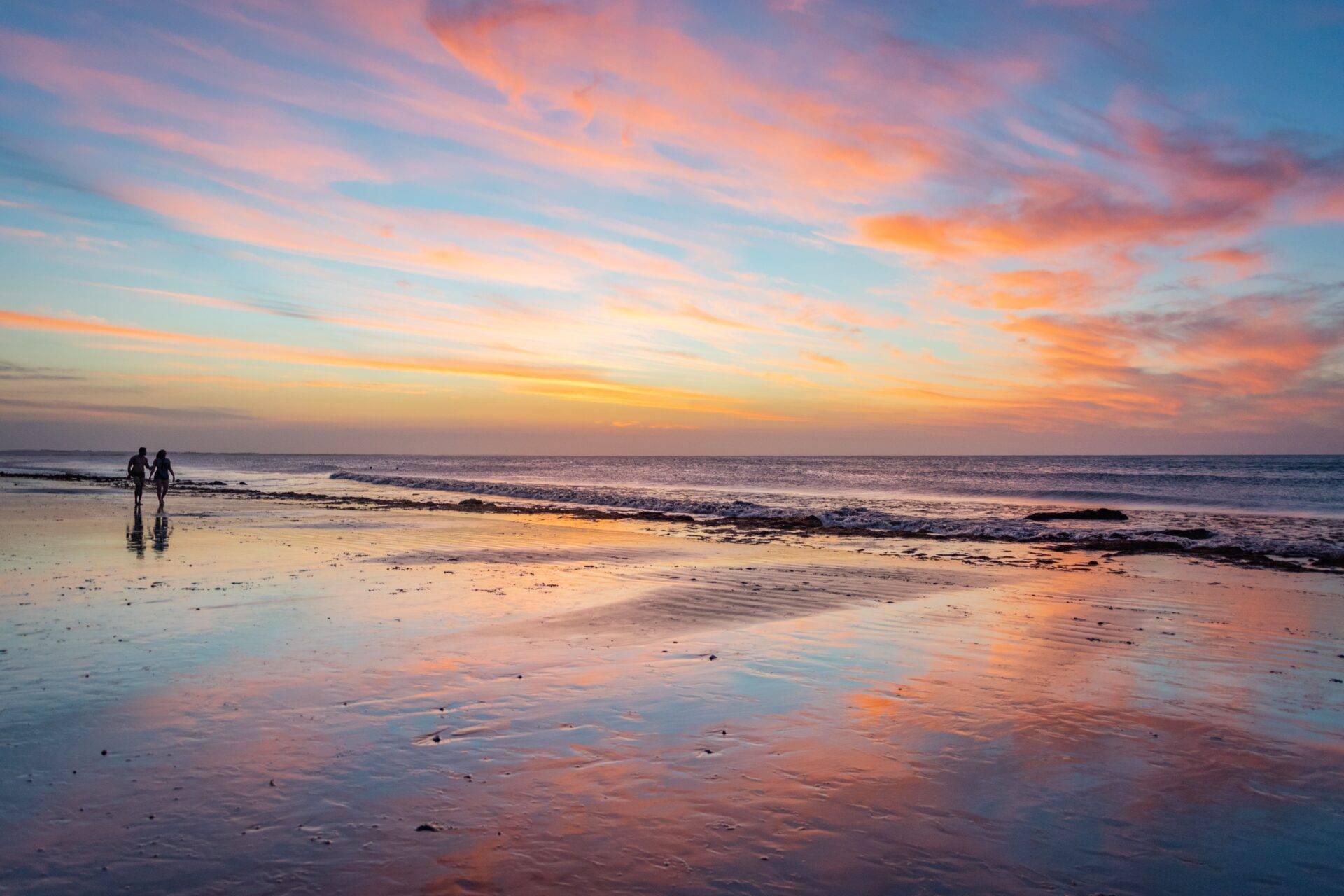 Deux surfeurs sur une plage au coucher de soleil avec reflets dorés sur le sable mouillé
