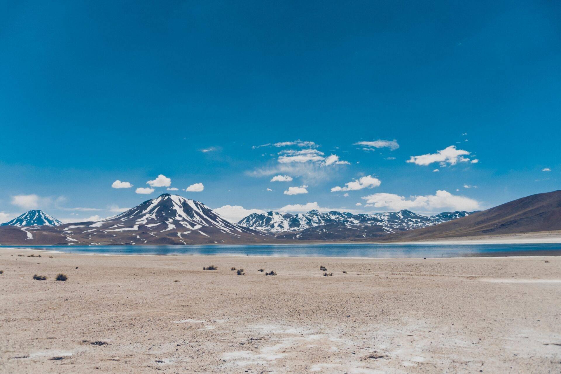 Désert de haute altitude avec lac turquoise et volcans enneigés sous ciel bleu dégagé