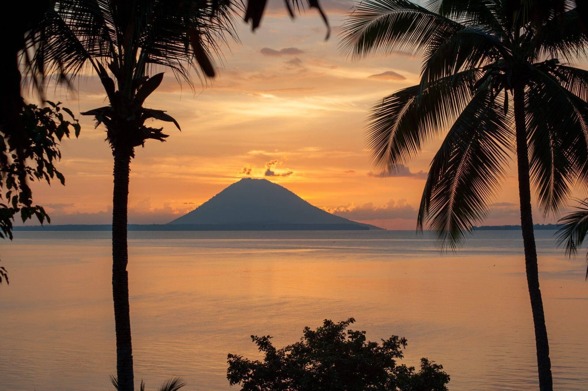 Coucher de soleil tropical sur un volcan en mer encadré par des palmiers silhouettés