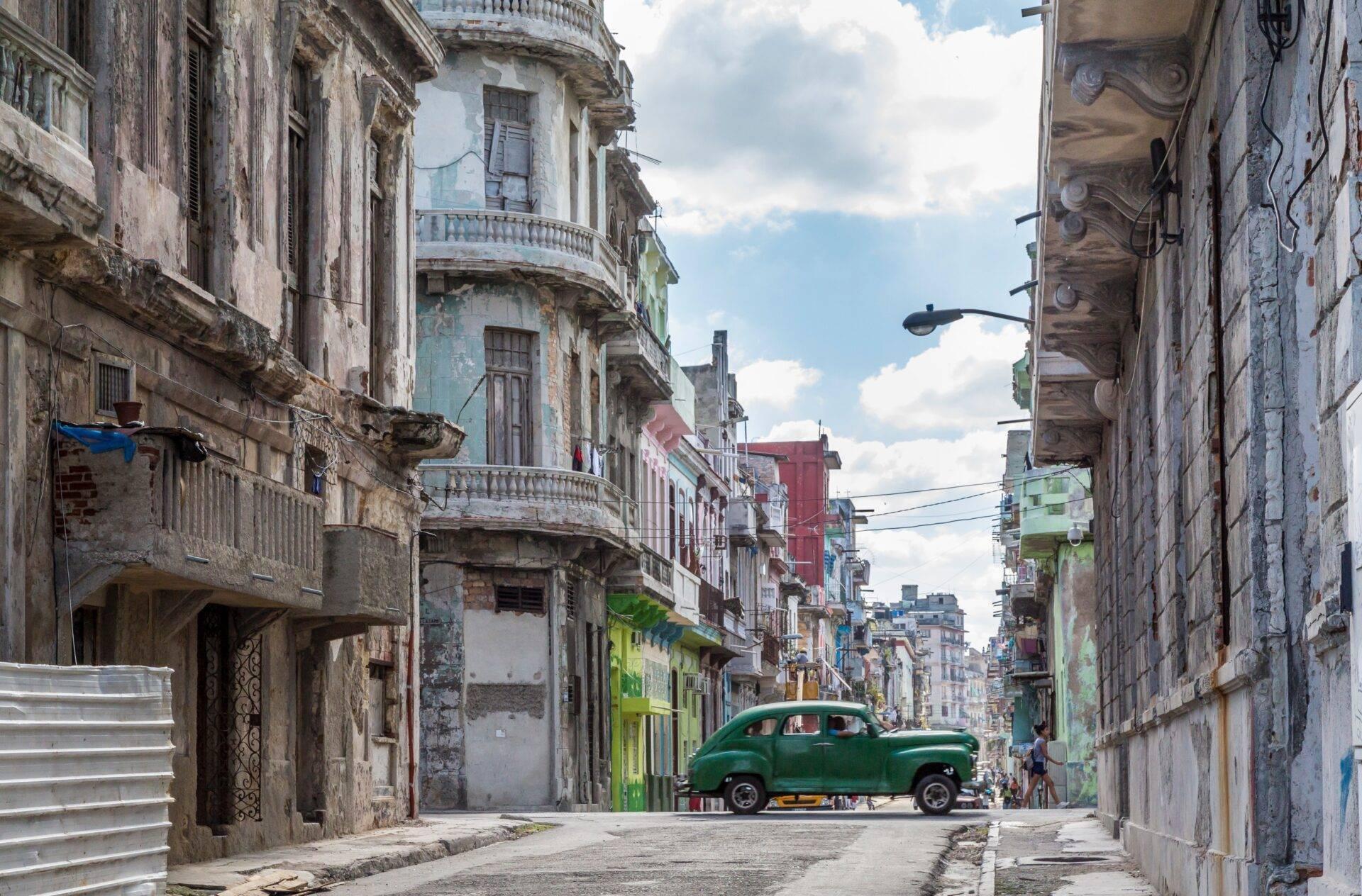 Une rue historique étroite aux façades coloniales colorées avec une vieille voiture verte garée