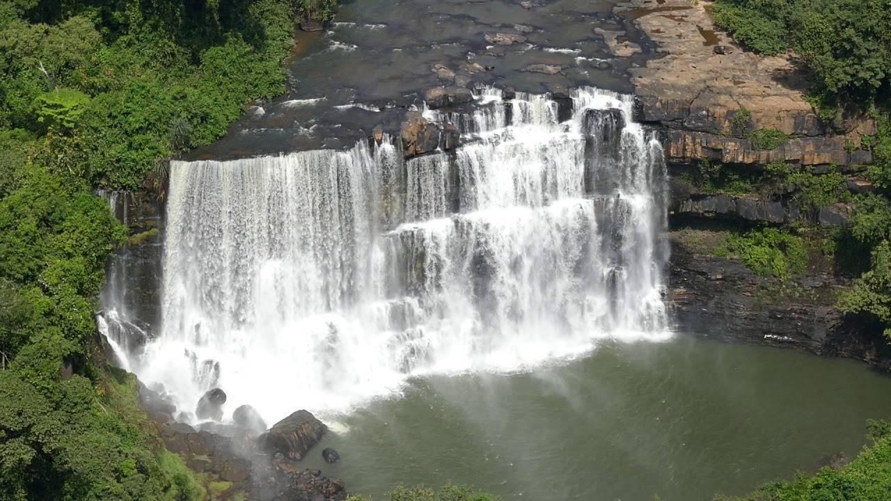 Une majestueuse cascade multi-étages déverse ses eaux blanches écumantes dans un bassin émeraude, encadrée de végétation tropicale luxuriante