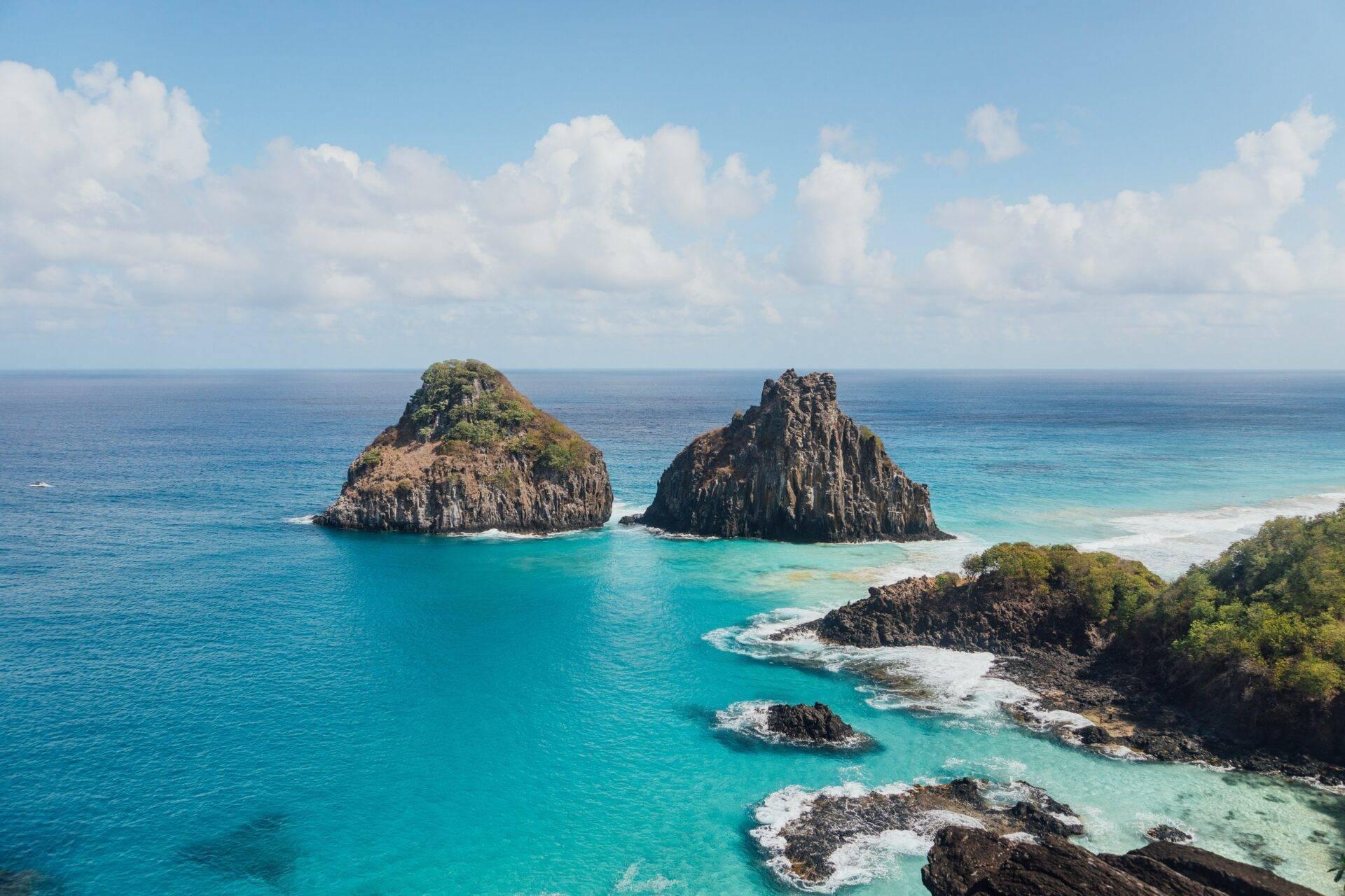 Formations rocheuses dramatiques émergeant d’une eau turquoise cristalline avec plage et végétation tropicale